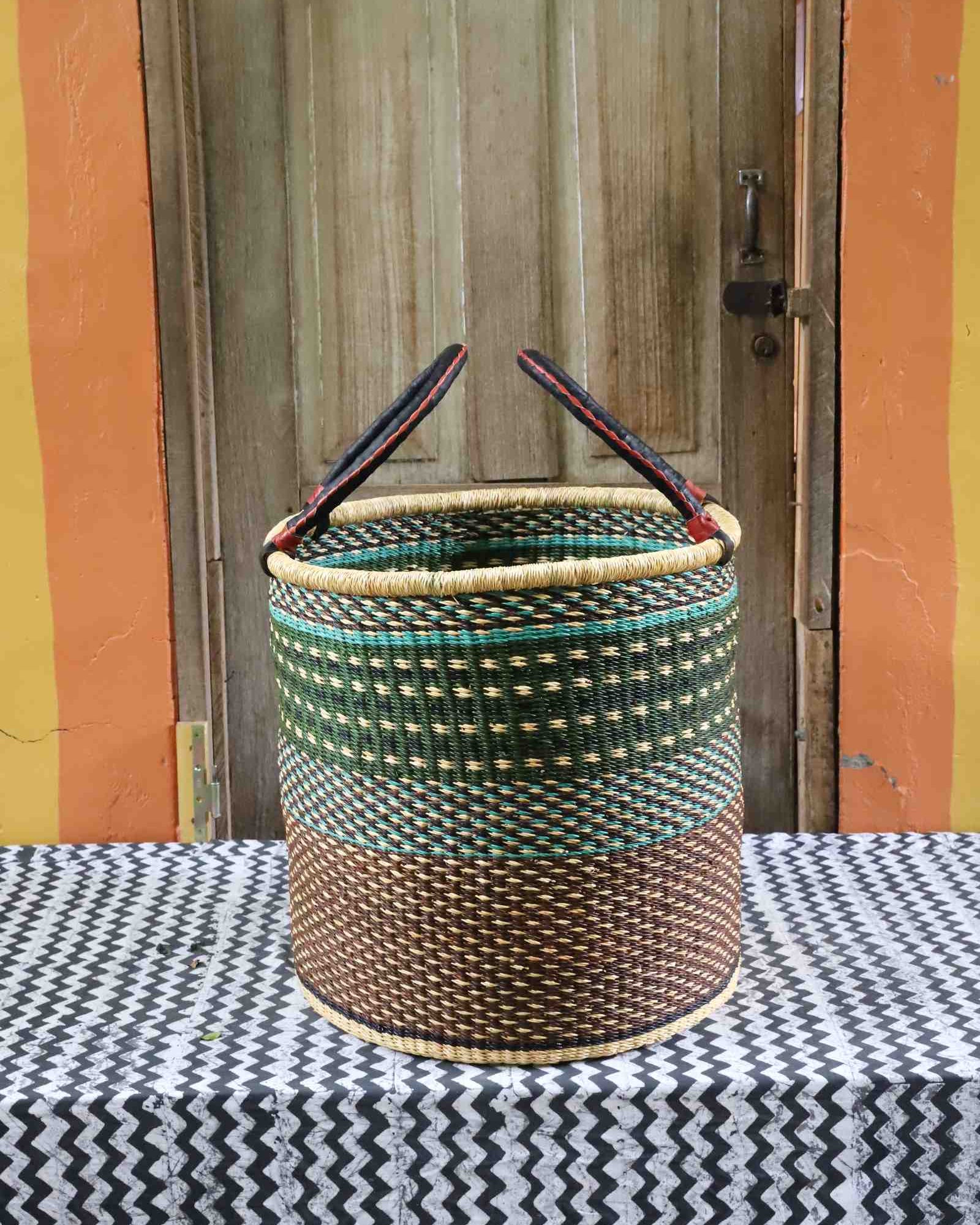 Large open laundry basket in green checkered weave with a dark brown base, styled on a chevron cloth.