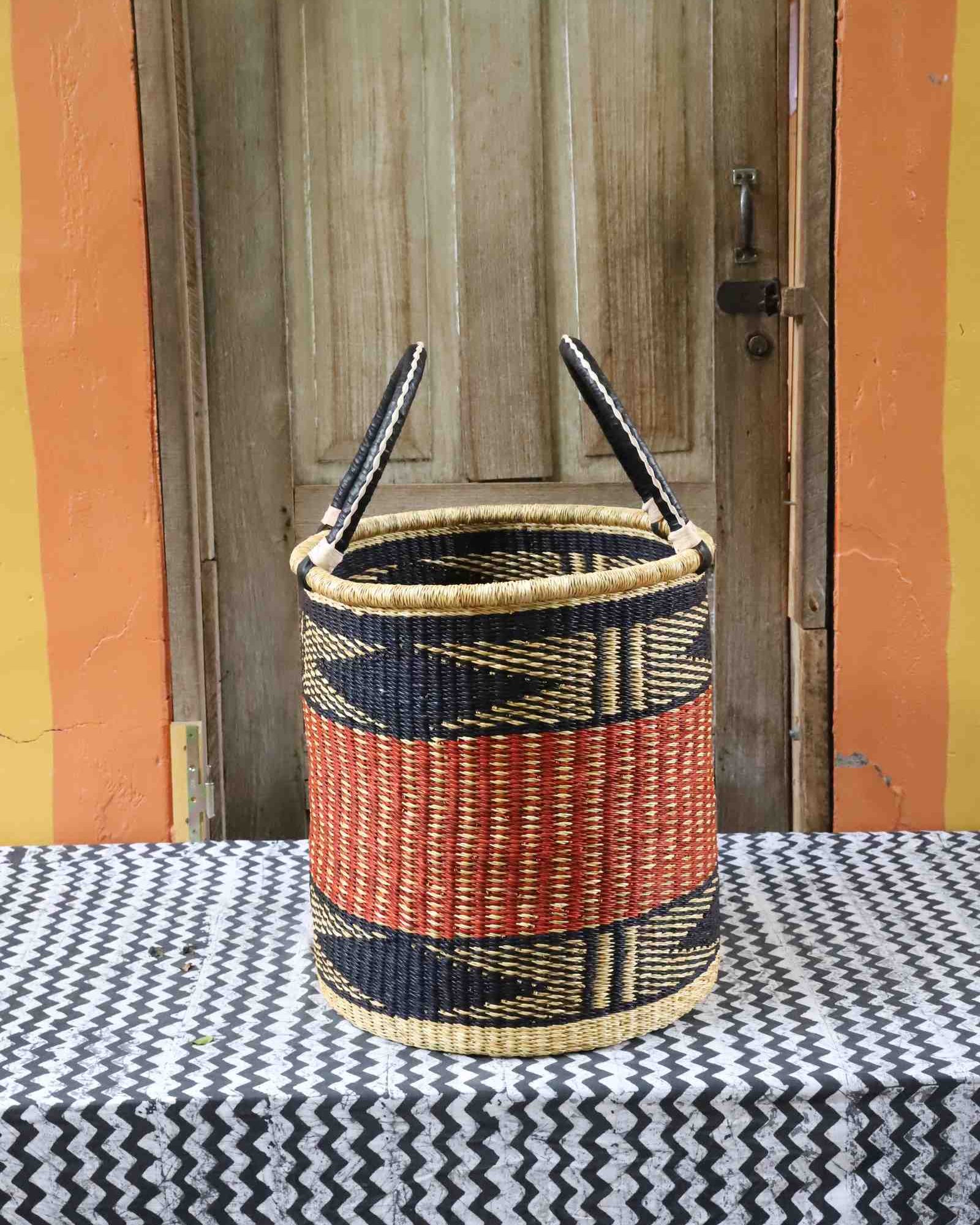 Open laundry basket in natural straw with an orange and black zigzag band, styled on a chevron cloth by a wooden door.