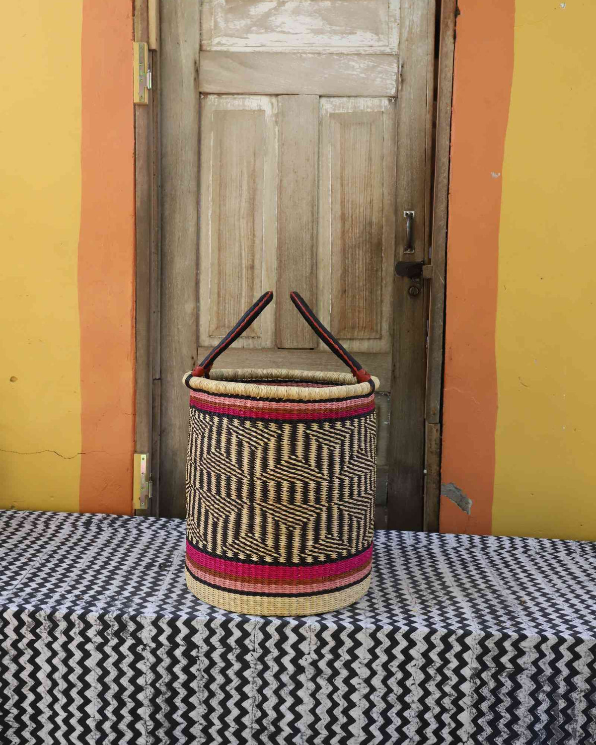 Small handwoven open-top Bolga laundry basket in natural straw with red bands and fine dark weave.