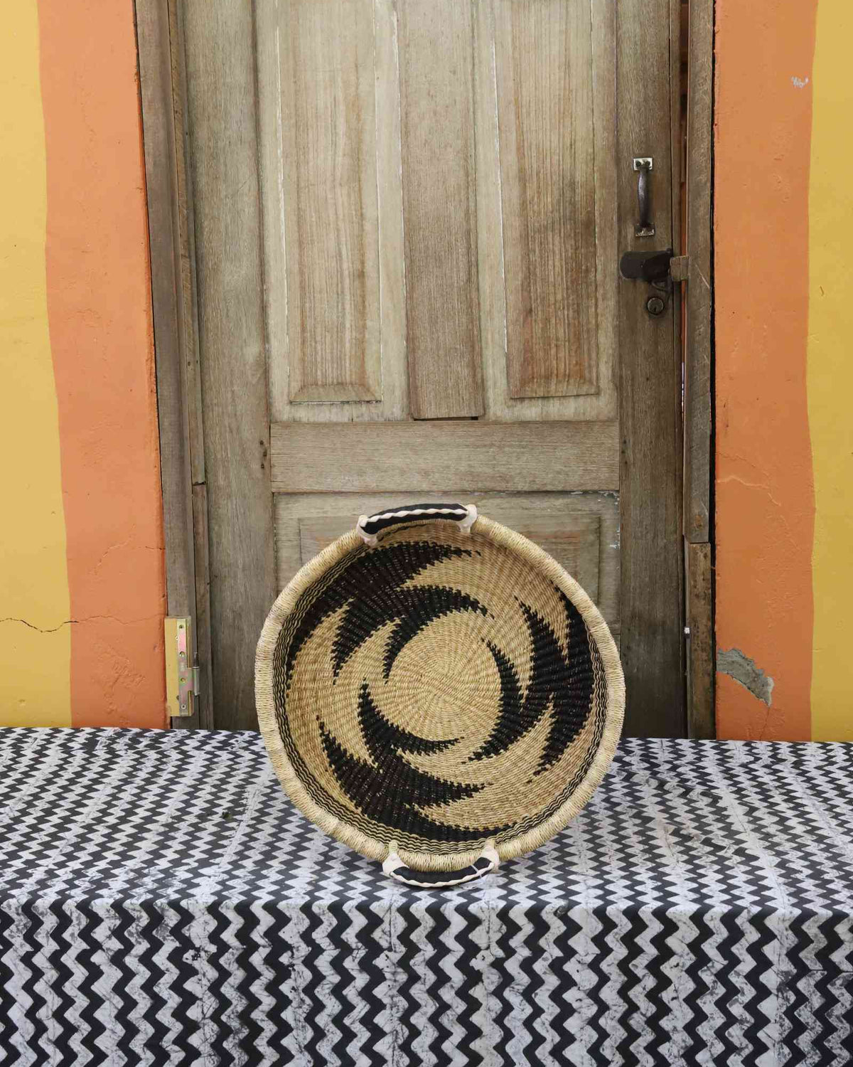 Handwoven Bolga wall tray disc in natural straw with a bold black star pinwheel pattern.