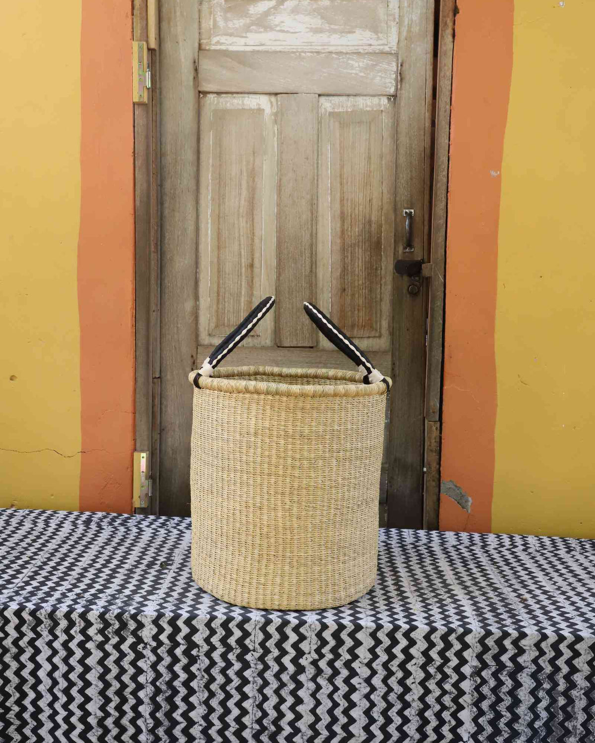Small handwoven open-top Bolga laundry basket in plain natural straw with twin looped handles.
