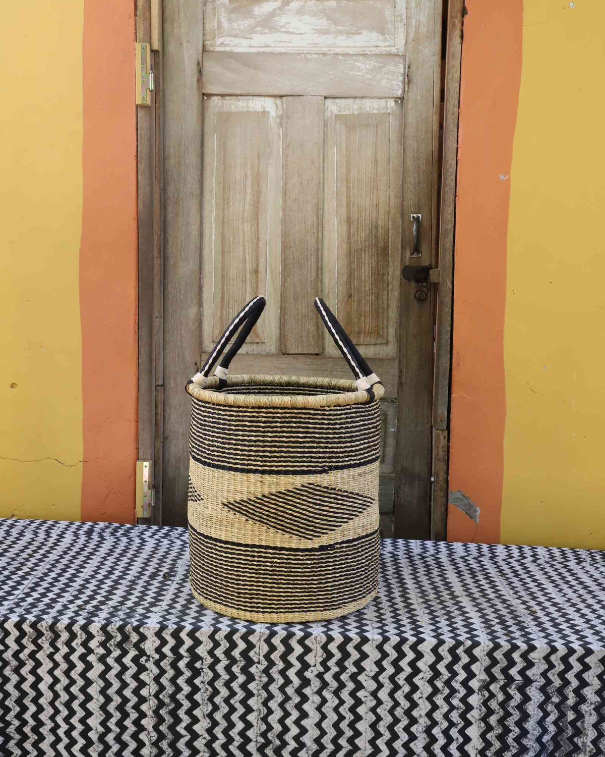 Large handwoven open-top Bolga laundry basket in natural straw with a dark diamond motif on the front.