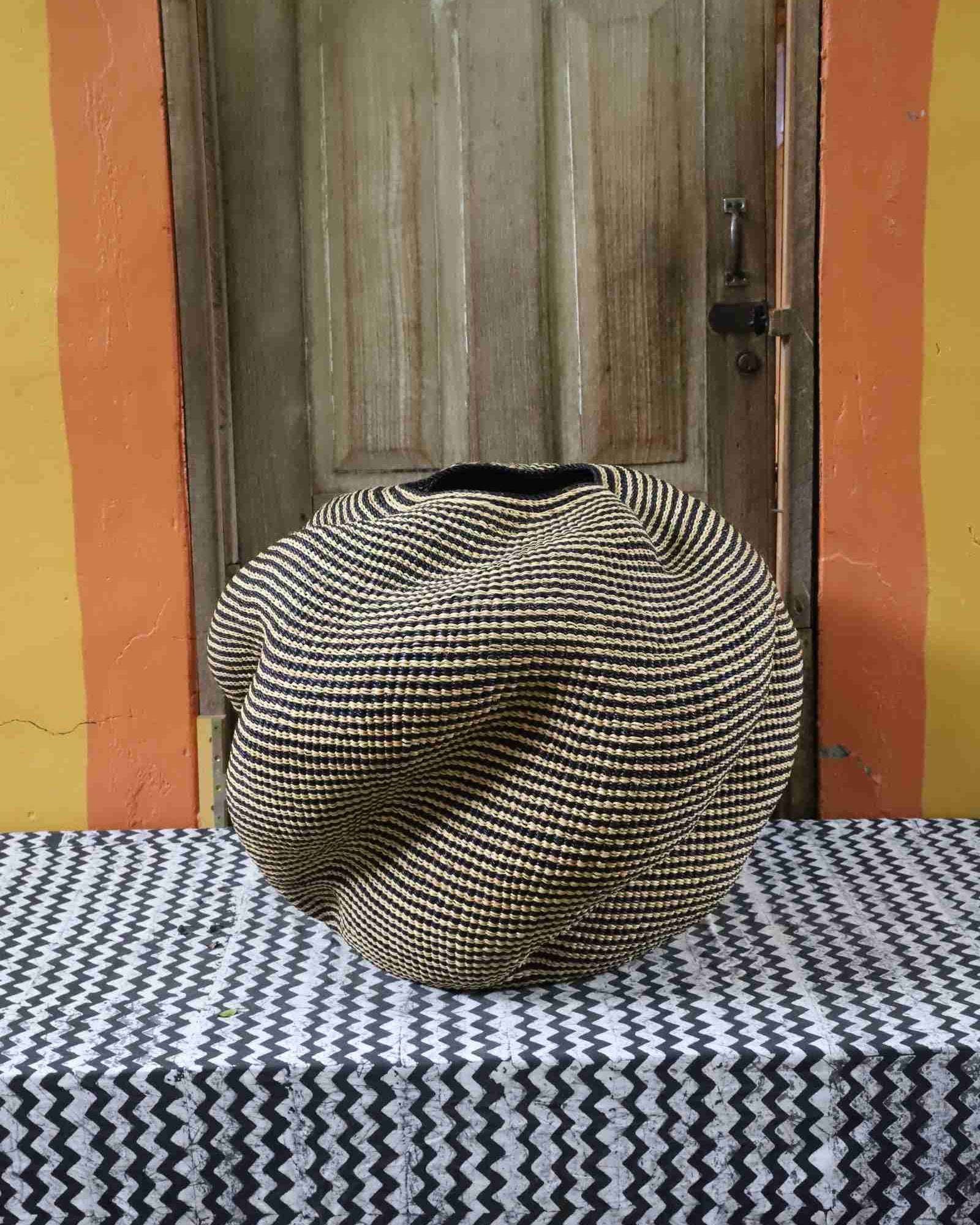 Large nest-shaped Bolga art basket in natural straw with a densely ridged weave, styled on a chevron cloth by a wooden door.