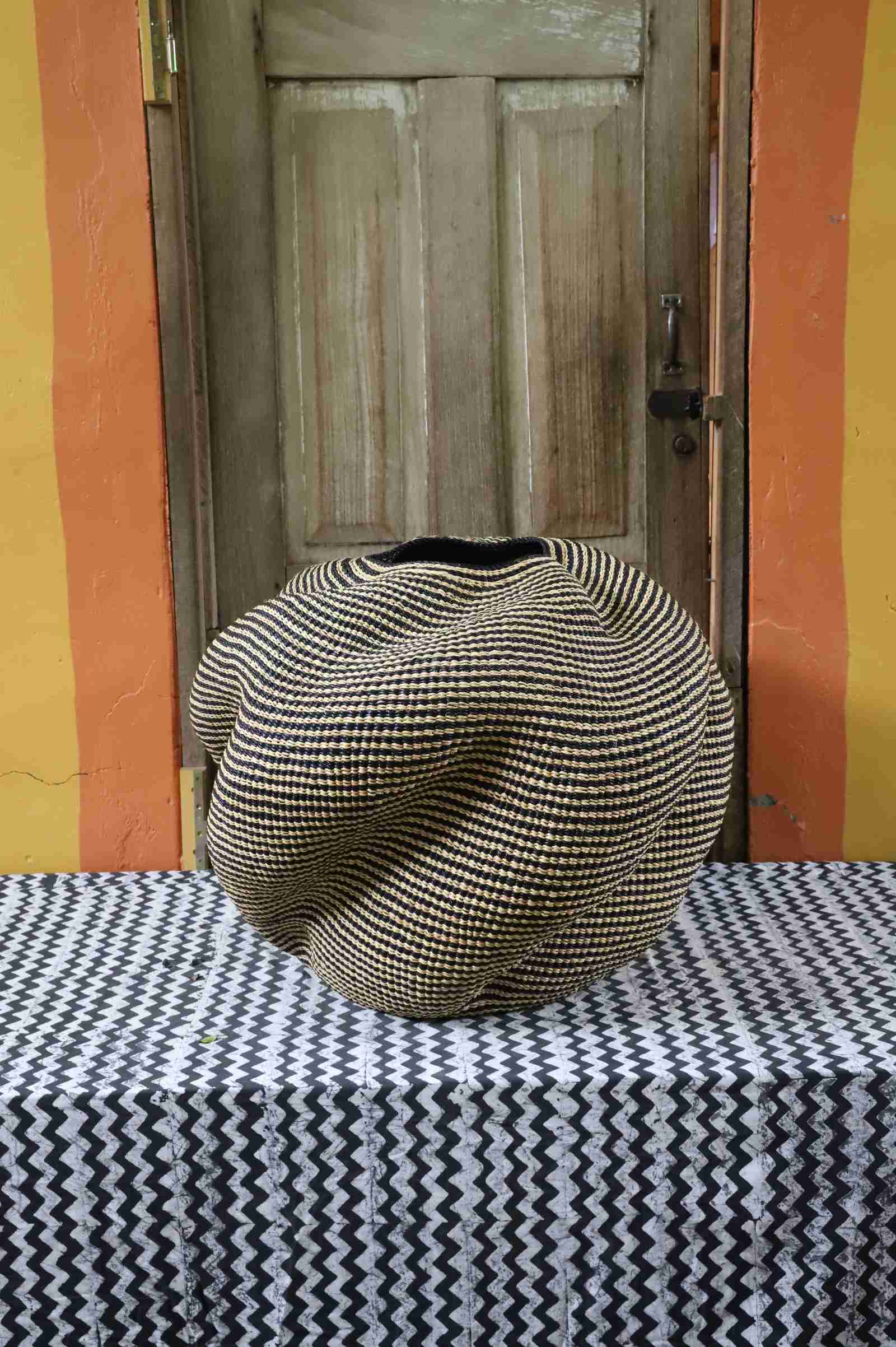 Large nest-shaped Bolga art basket in natural straw with a densely ridged weave, styled on a chevron cloth by a wooden door.
