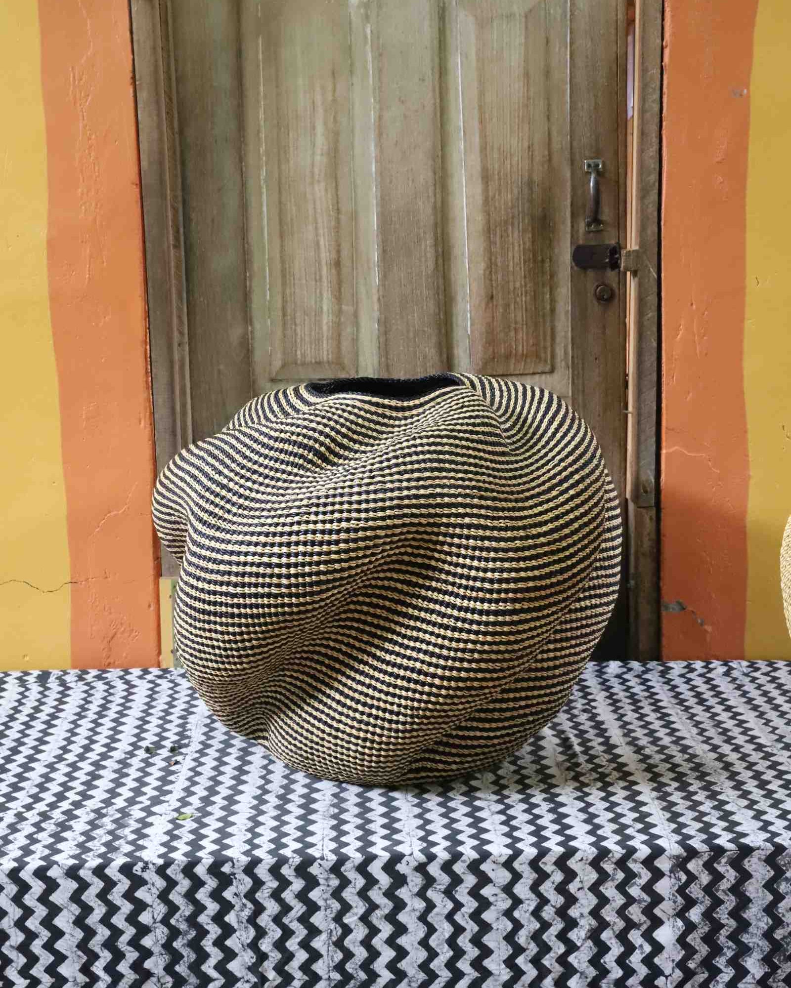 Large nest-shaped Bolga art basket in natural straw with a densely ridged weave, front view on a chevron cloth.