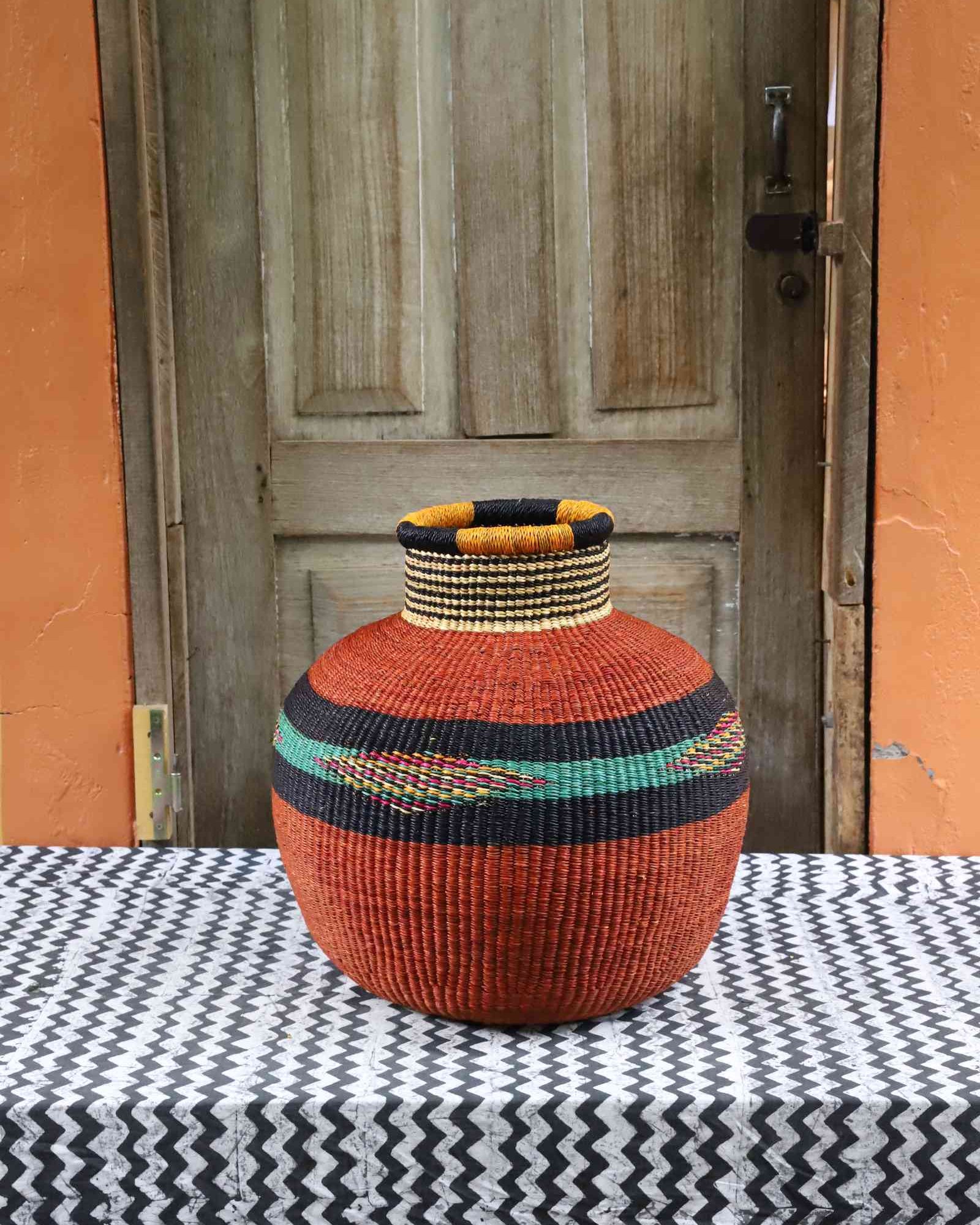 Round Bolga basket in terracotta with a black and cream striped neck and a green diamond-patterned band.