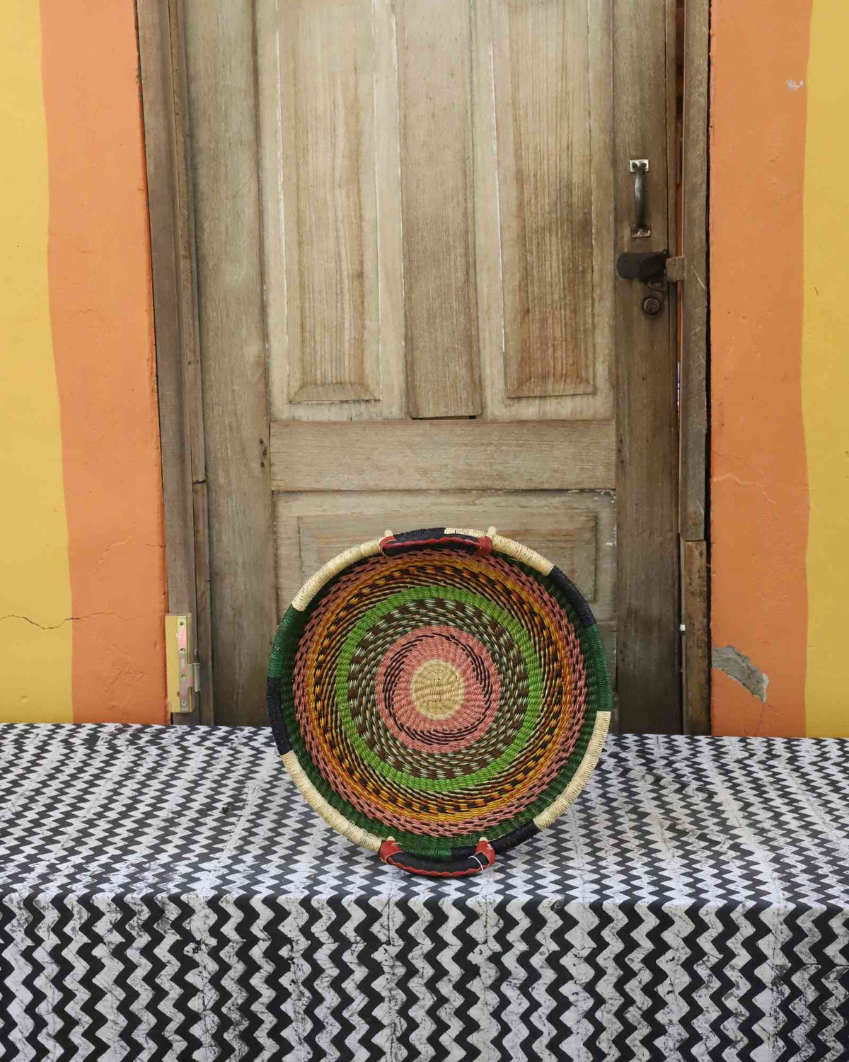 Handwoven Bolga wall tray disc in natural straw with red, green and orange banded rings.