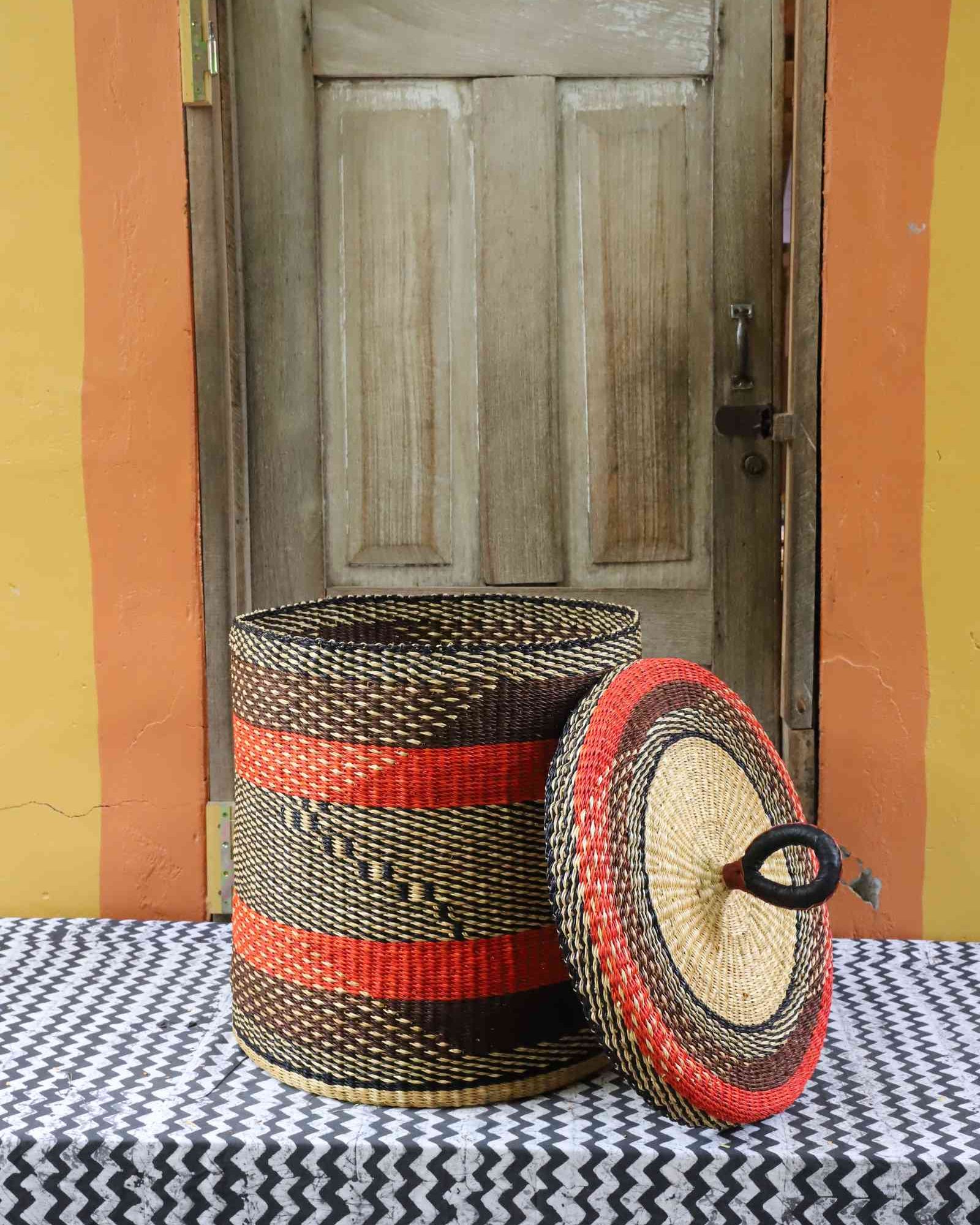Handwoven Bolga laundry basket with lid removed, showing red and black banded body and matching woven lid.