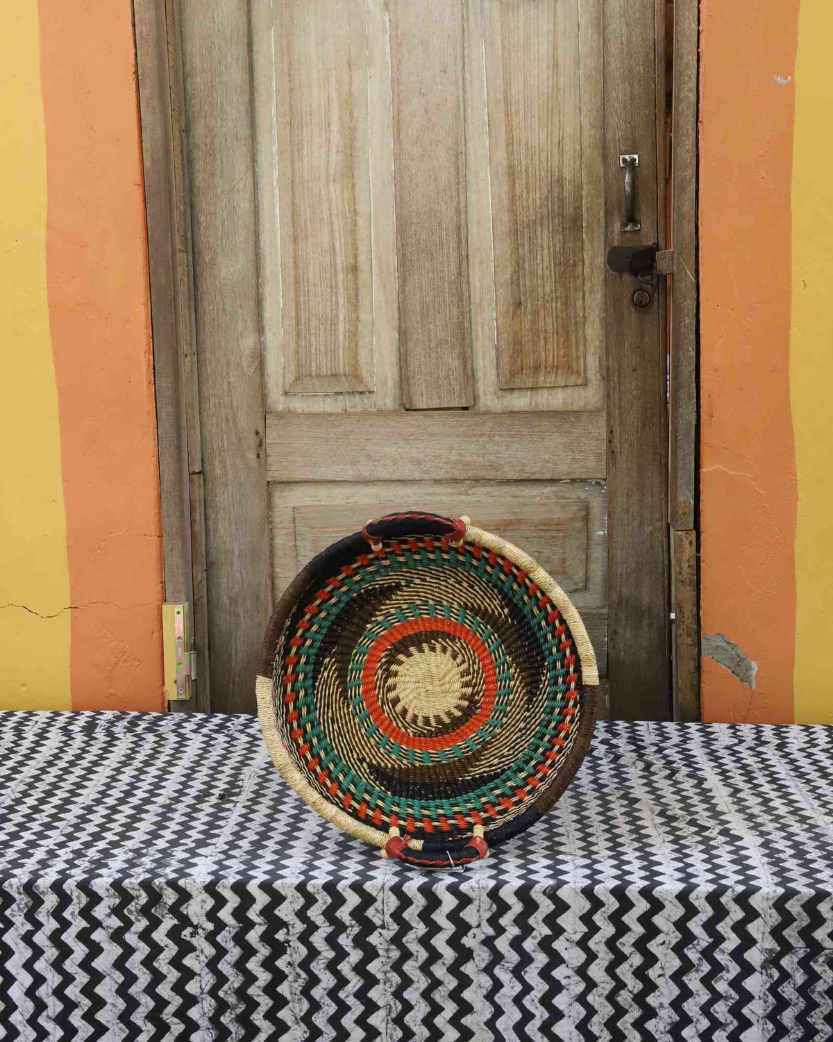 Handwoven Bolga wall tray disc with dark rim, green and orange concentric bands and yellow centre.