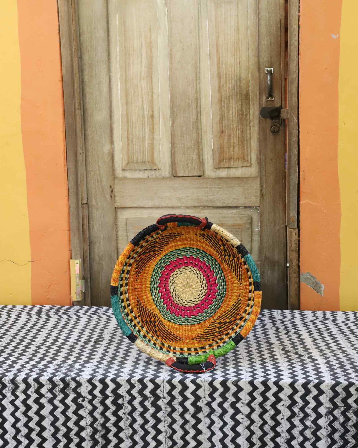 Handwoven Bolga wall tray disc with fine yellow, pink and black concentric bands.