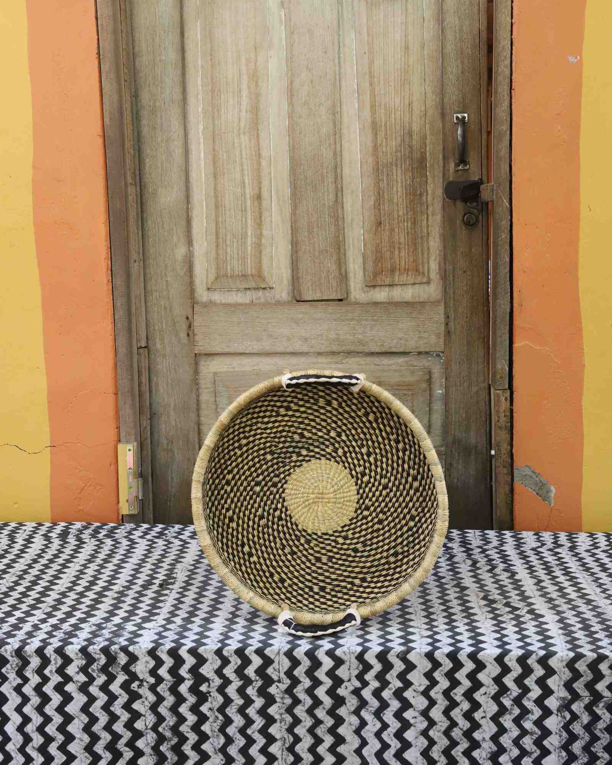 Handwoven Bolga wall tray disc in dark straw with a yellow centre dot.