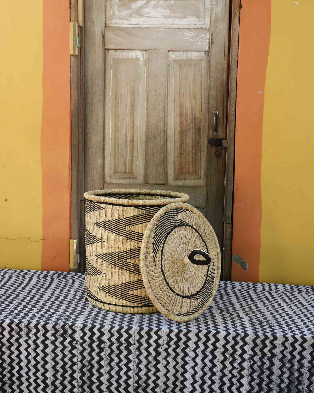 Handwoven Bolga laundry basket with lid removed, natural body with black wave motif and matching coiled lid.