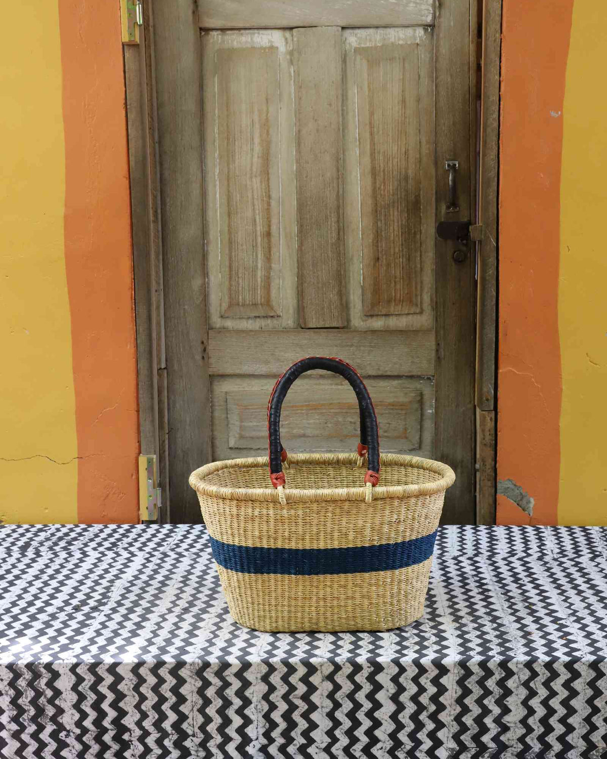 Small handwoven Bolga Zaane Tia market basket in natural straw with a navy blue band and twin leather handles.