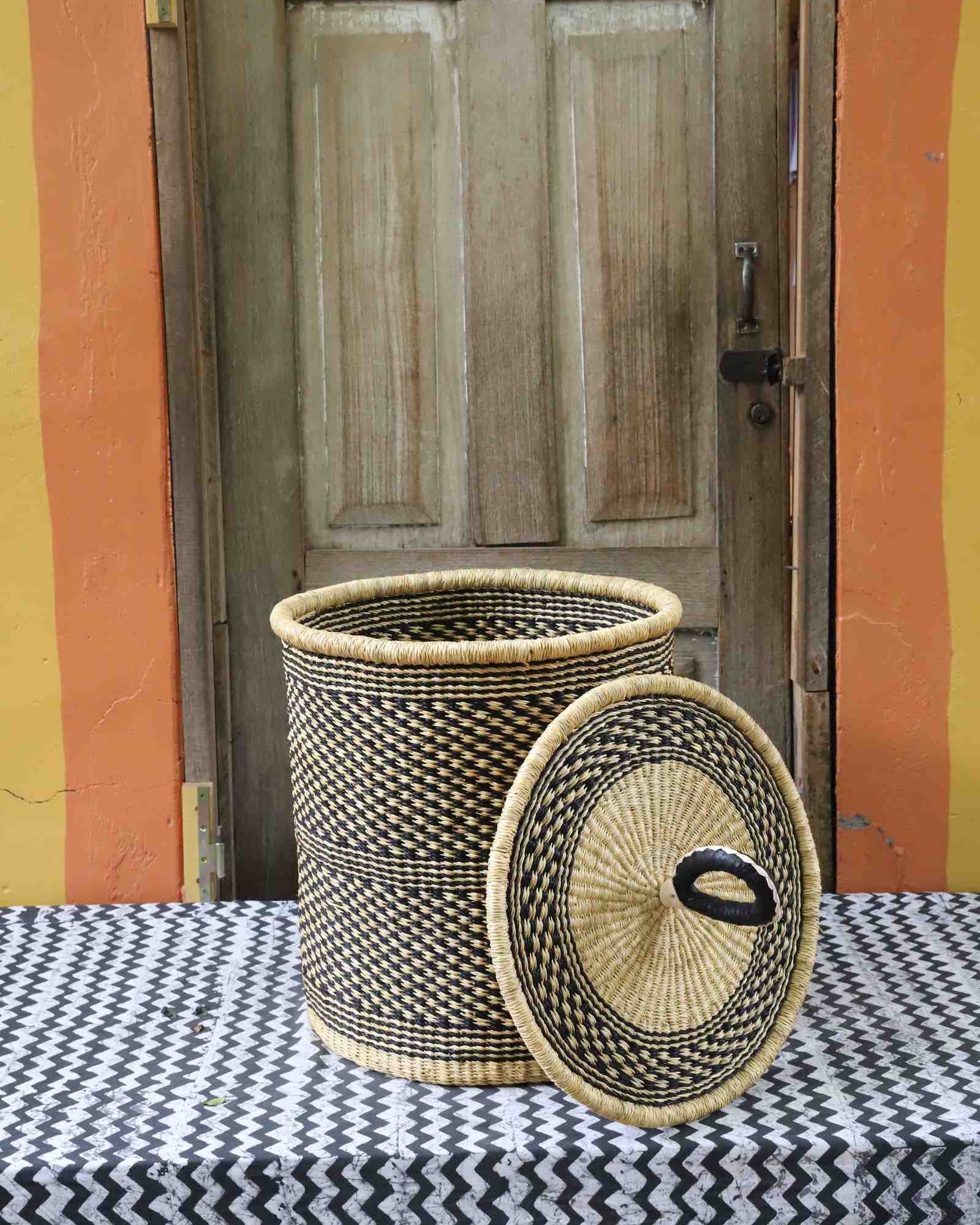 Coiled-rim laundry basket in a black and tan speckled weave, lid resting alongside on a chevron cloth.