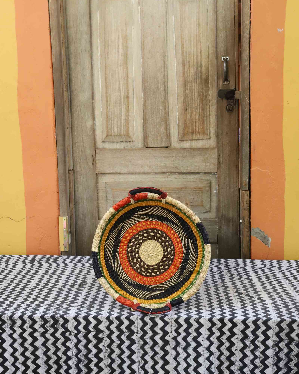 Handwoven Bolga wall tray disc with natural rim, orange and black concentric bands and yellow centre.