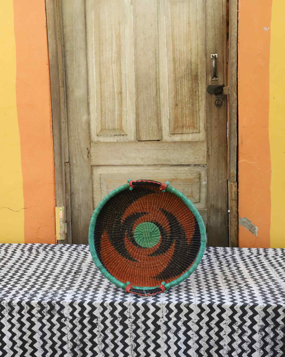 Handwoven Bolga wall tray disc with green rim, orange concentric bands and green centre.