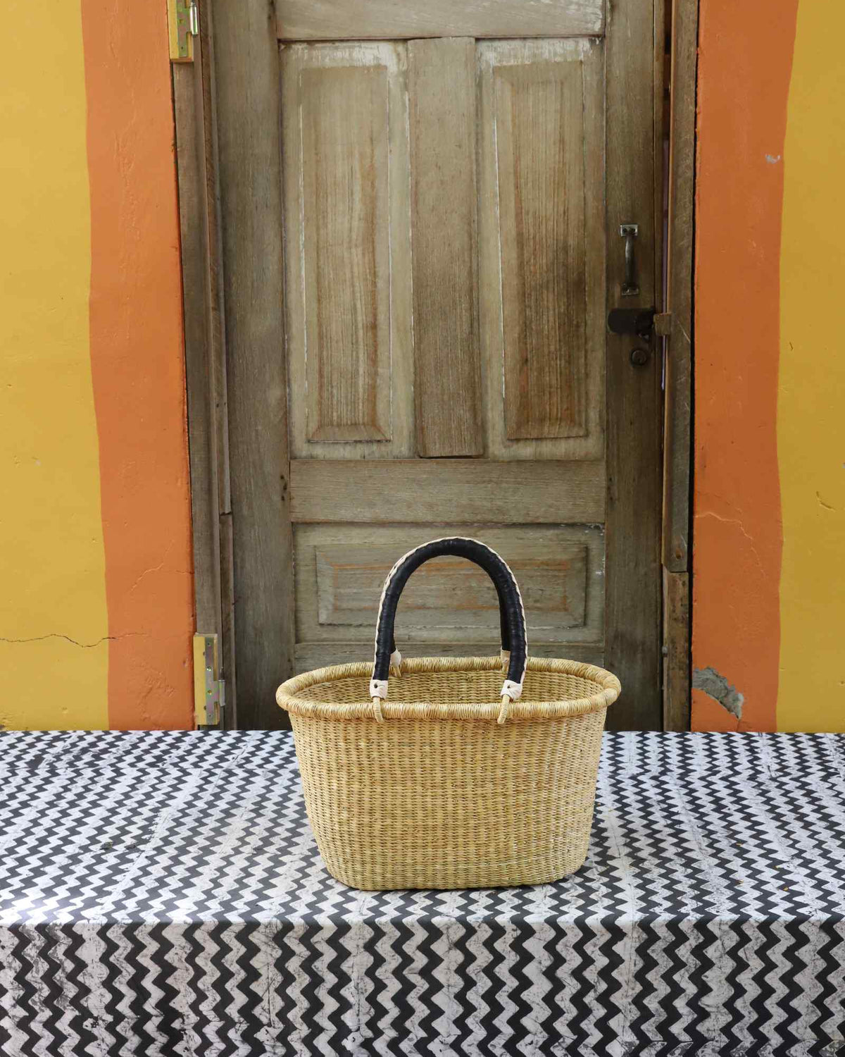 Small handwoven Bolga Zaane Tia market basket in plain natural straw with a dark leather-wrapped handle.