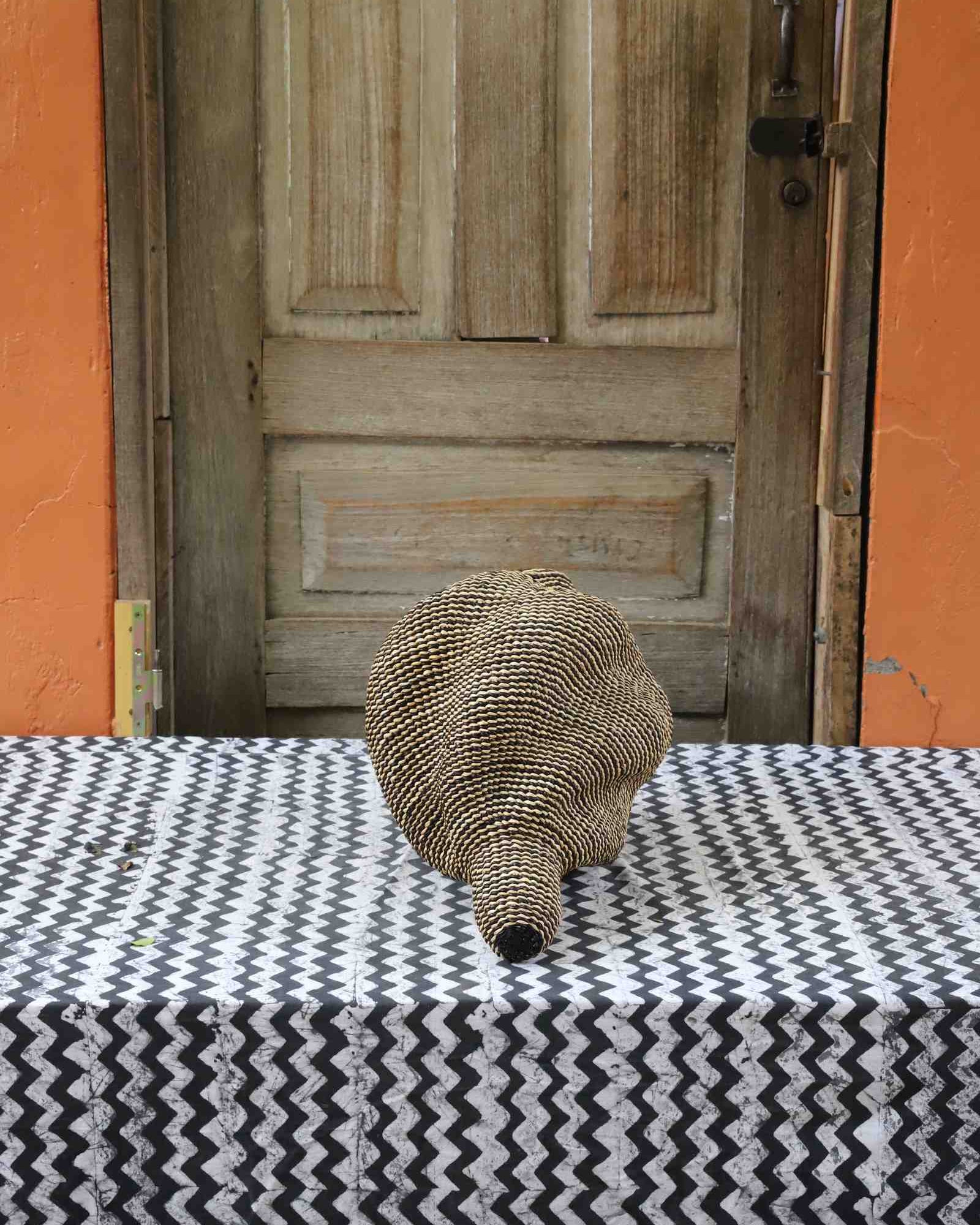 Small spiral-form Bolga art basket in natural straw, rear view on a chevron cloth.