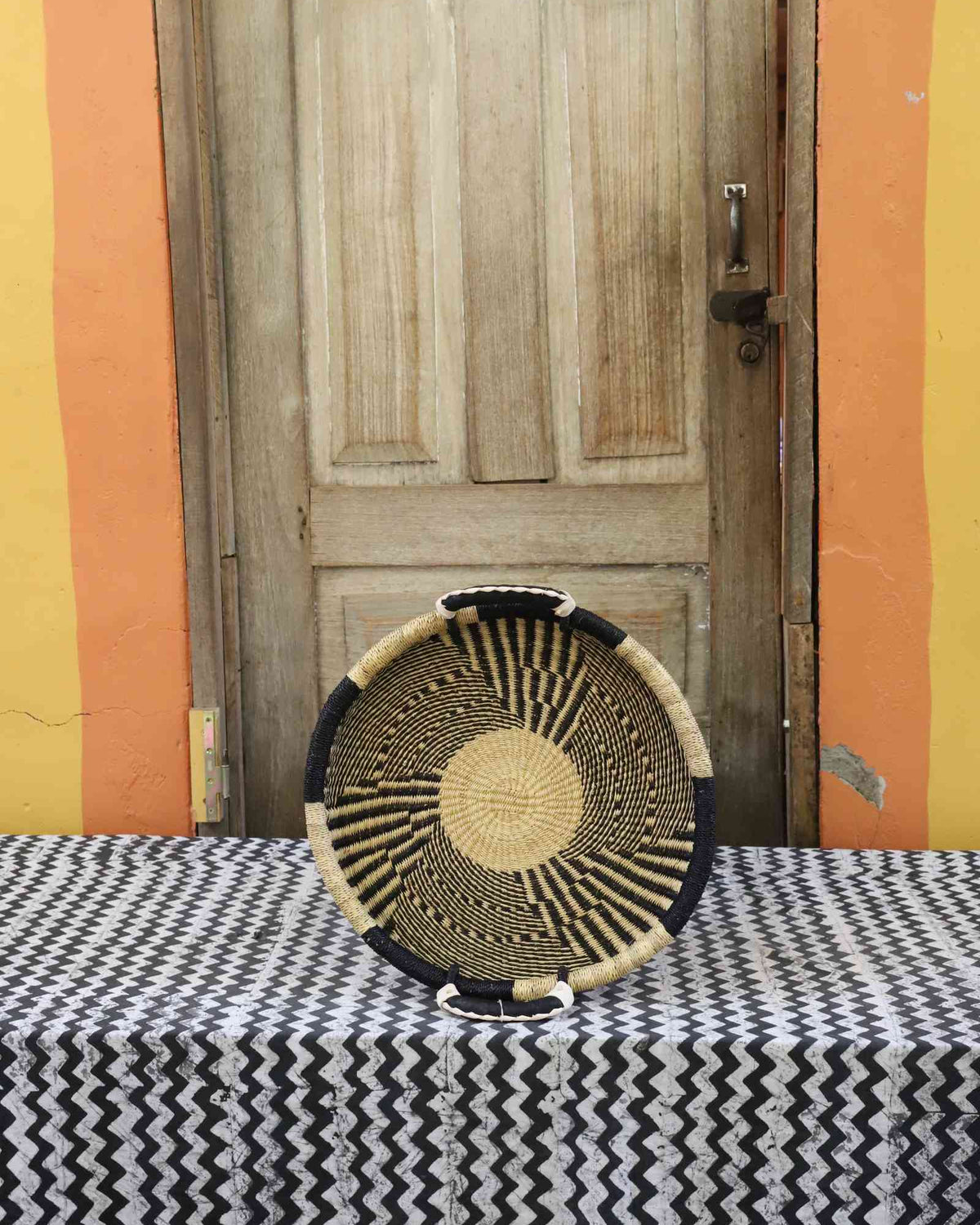 Handwoven Bolga wall tray disc in dark straw with fine radial stripes and a natural centre.