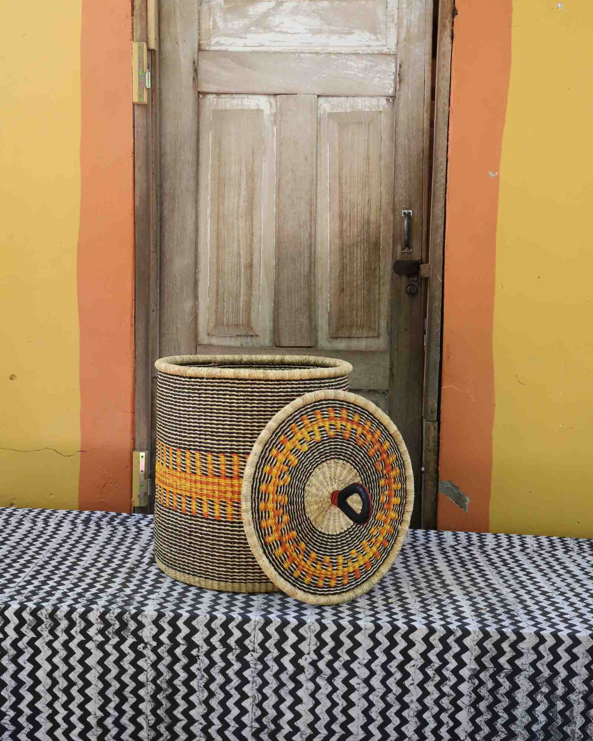 Handwoven Bolga laundry basket with lid removed, natural body with orange band and multicolour rim lid.