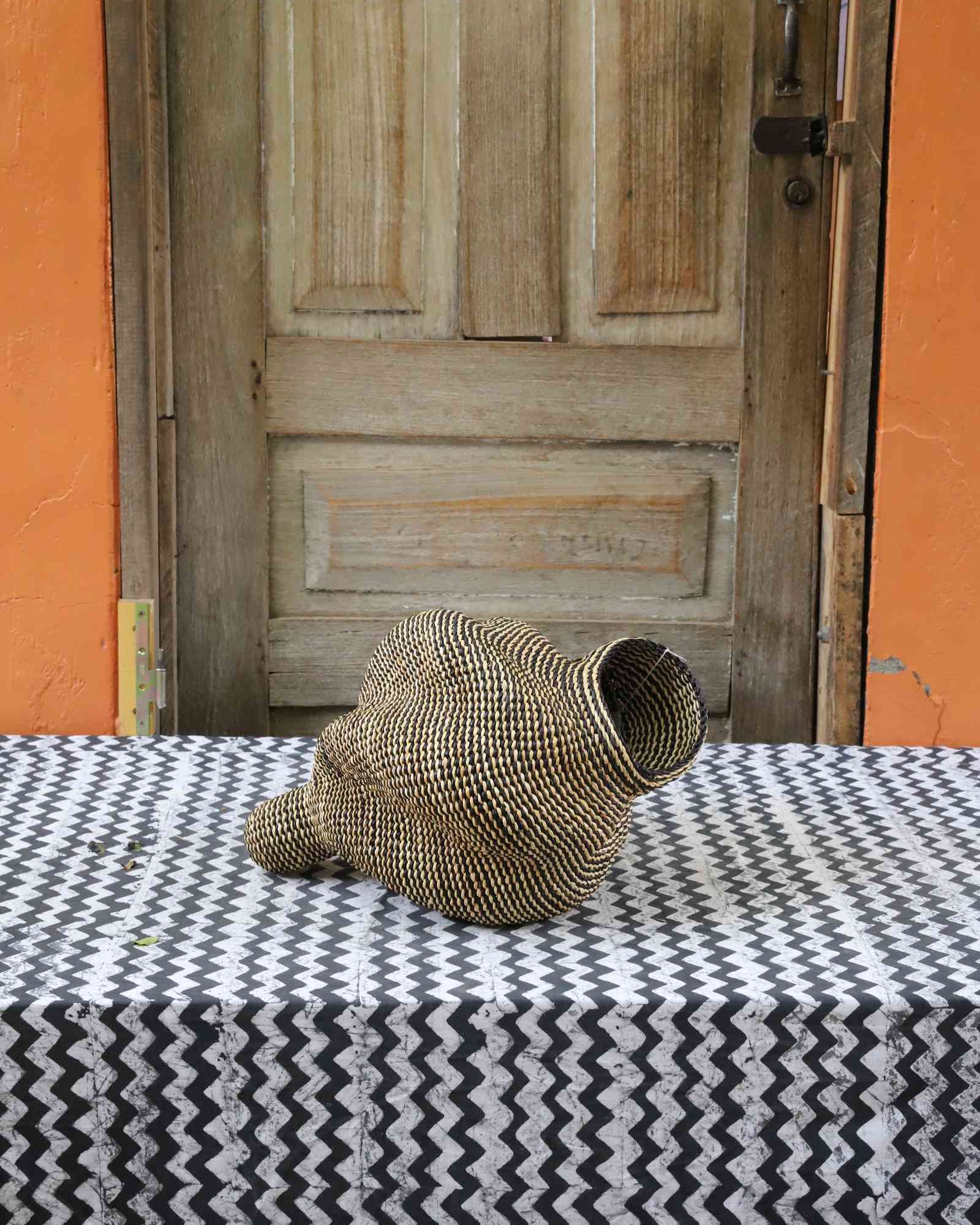 Small spiral-form Bolga art basket in natural straw, front view showing the curled tail detail.