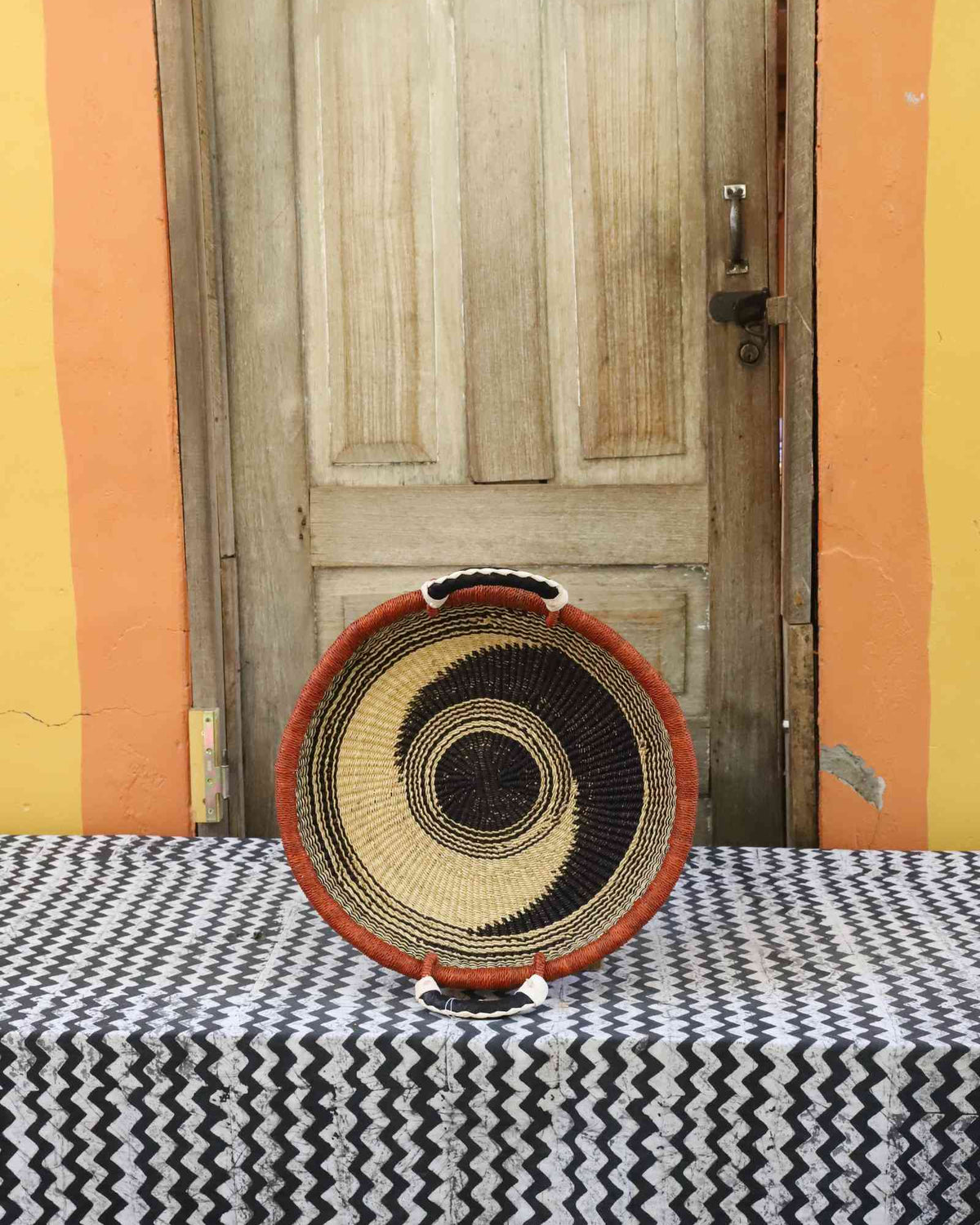 Handwoven Bolga wall tray disc with orange rim, black concentric rings and natural centre.