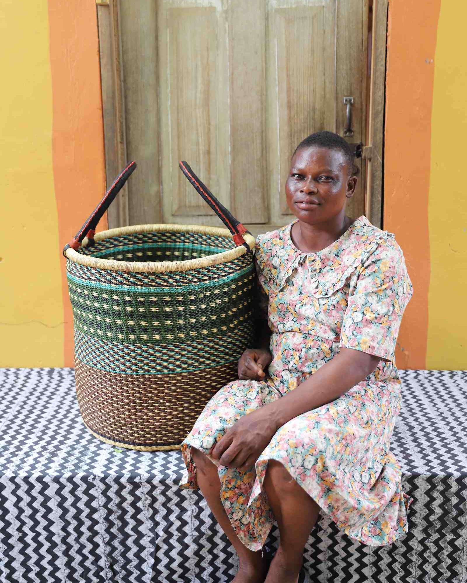 Large open laundry basket in green checkered weave with a dark brown base, held by a seated person for scale.