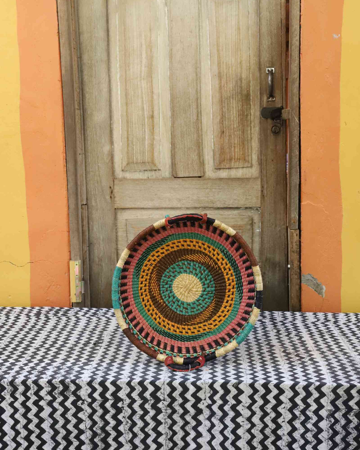 Handwoven Bolga wall tray disc with natural rim, red and green concentric bands and yellow centre.