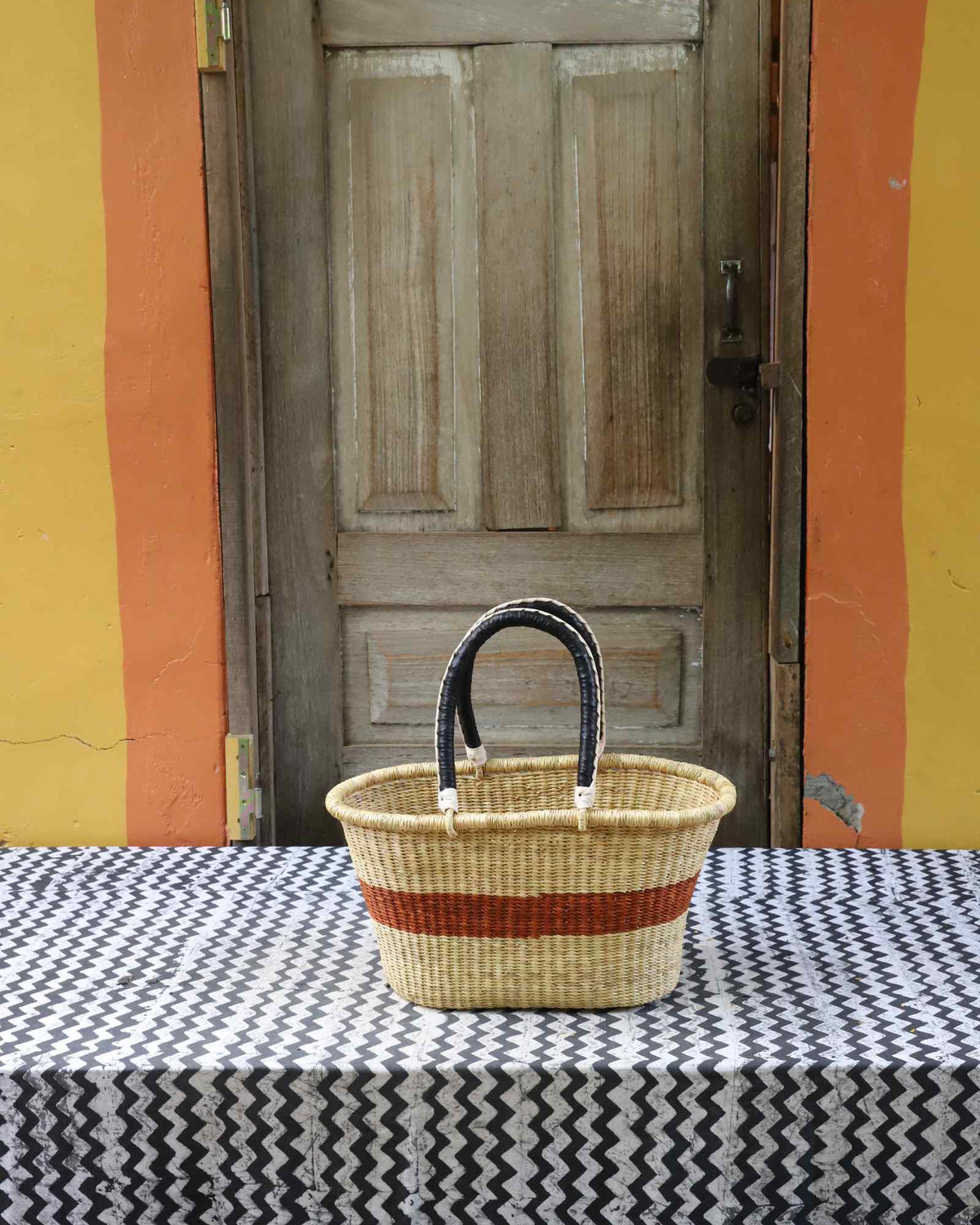 Small handwoven Bolga Zaane Tia market basket in natural straw with a rust-orange band and leather-wrapped handle.