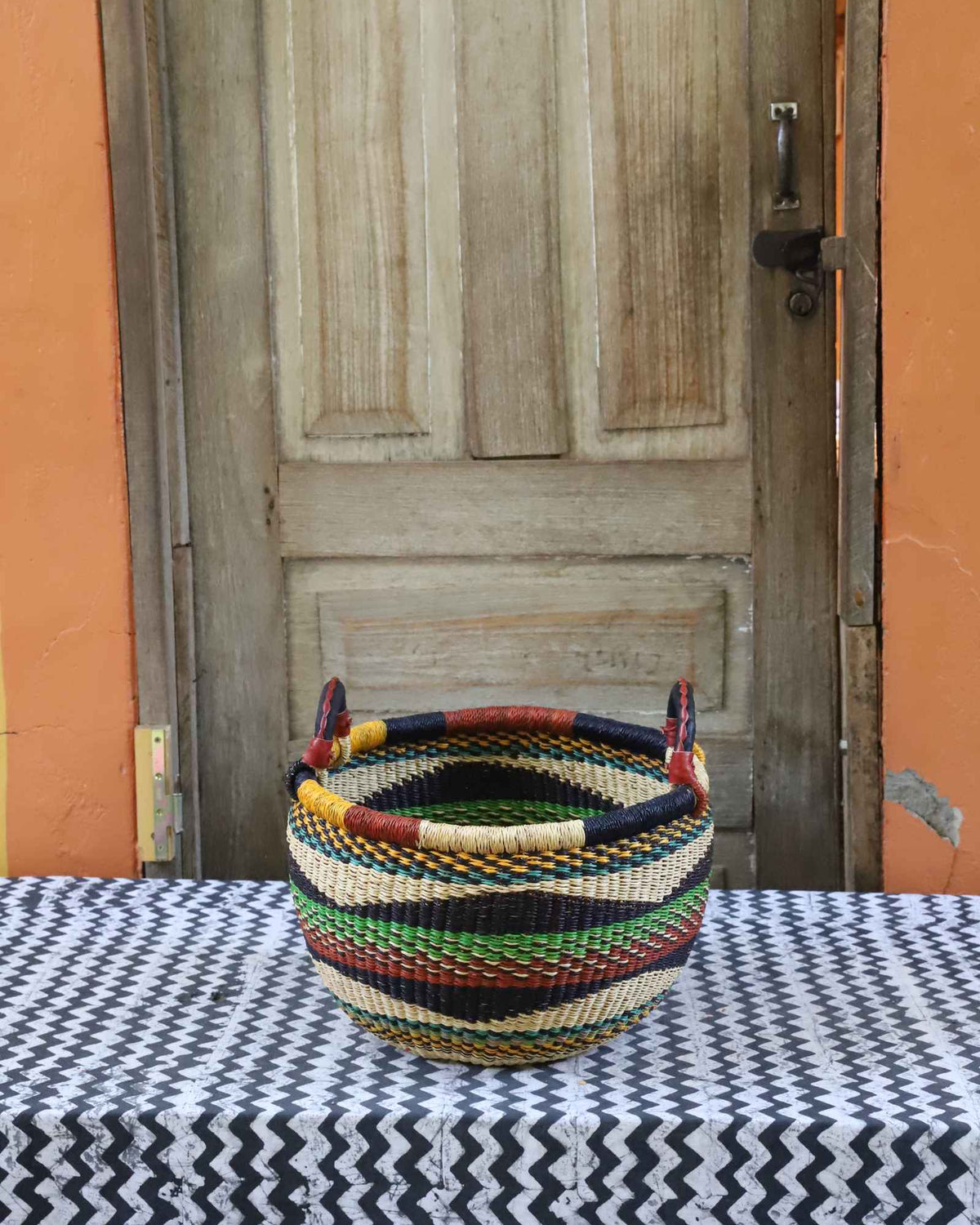 Small handwoven Bolga Gbenka storage basket with green, red, black and yellow banded stripes.