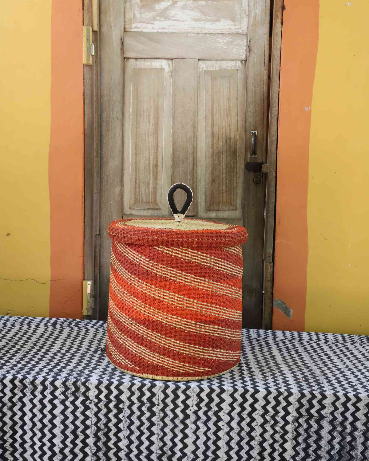 Handwoven Bolga laundry basket with lid dyed bold rust-orange with fine wavy stripes.