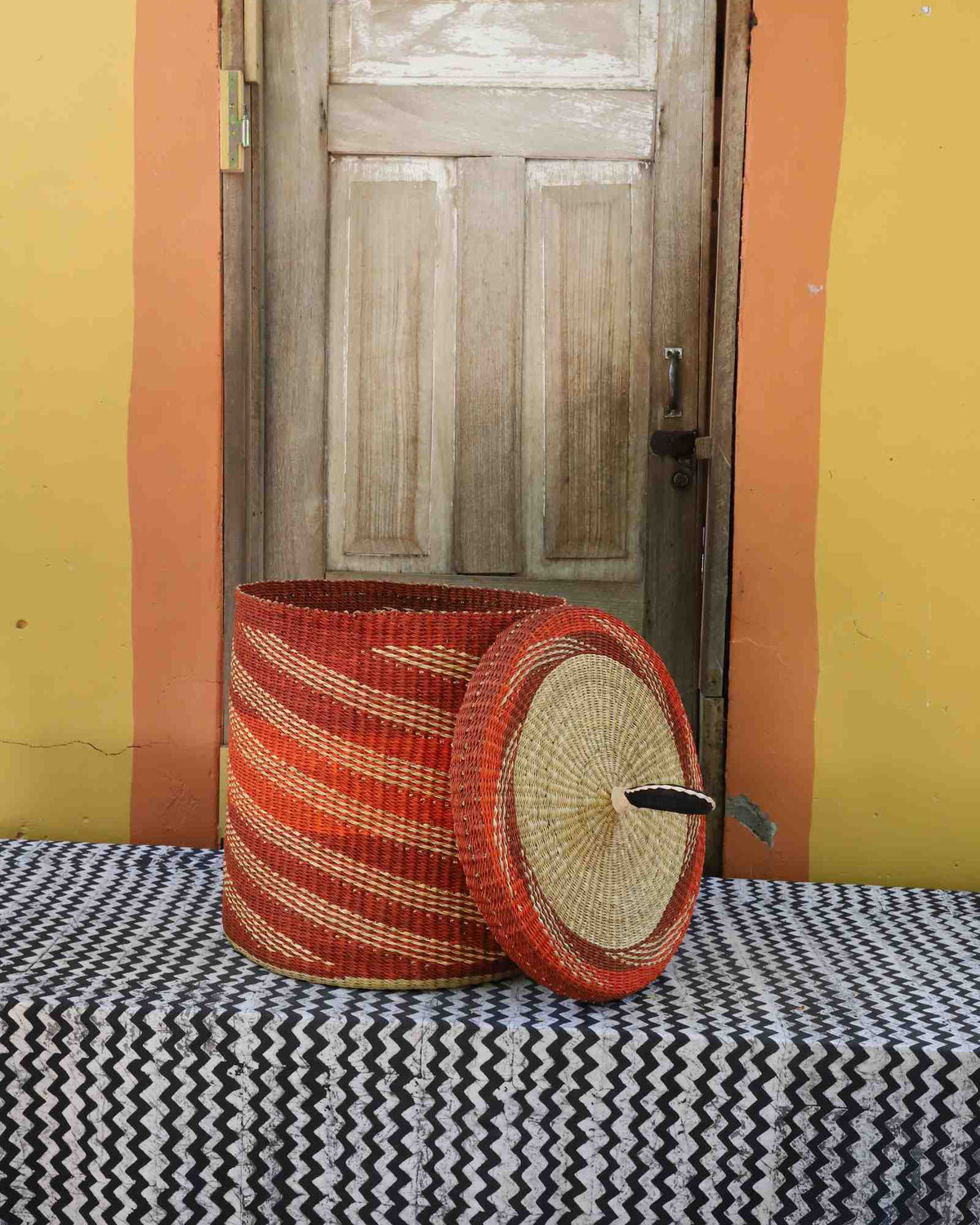 Handwoven Bolga laundry basket with lid removed, rust-orange body with fine wavy stripes and matching lid.