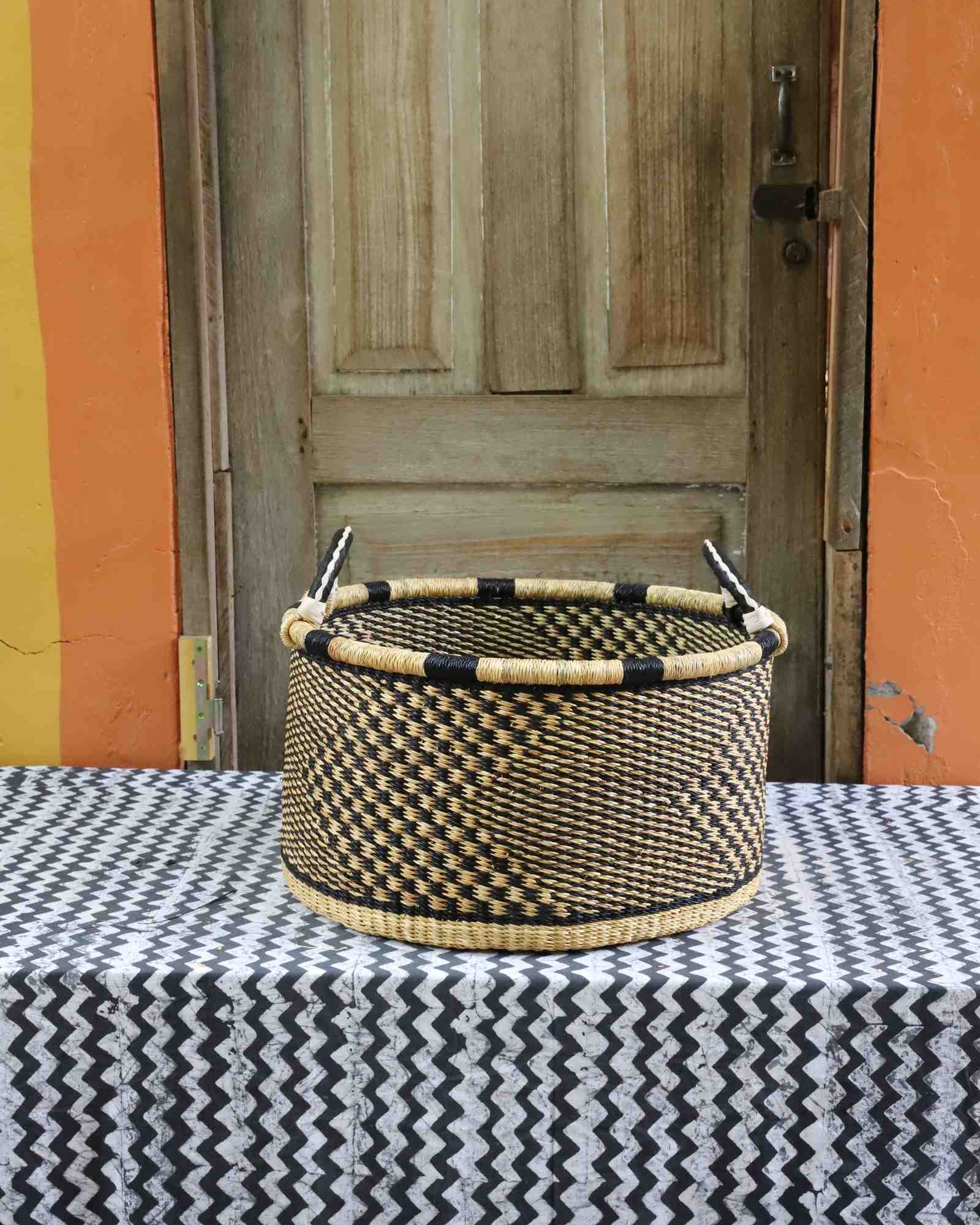 Handwoven Bolga storage basket in natural straw with a bold black geometric weave and twin handles.