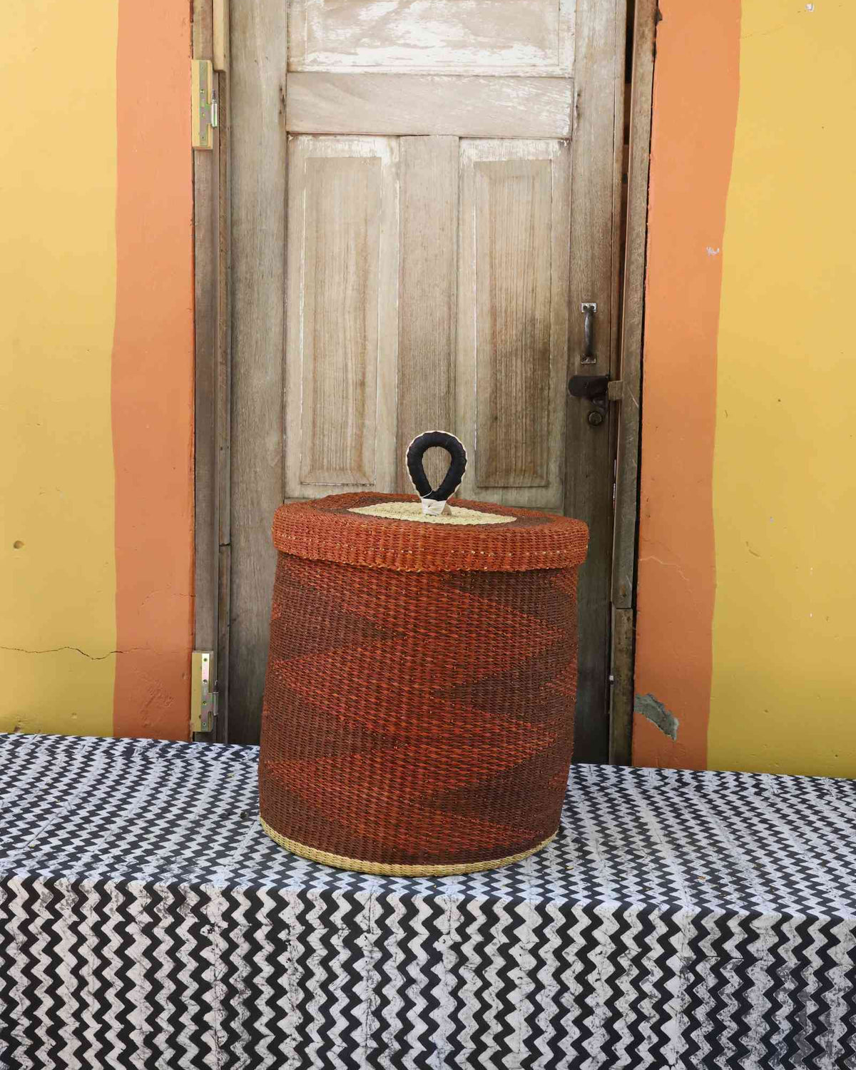 Handwoven Bolga laundry basket with lid dyed rust-red with a natural rim highlight.