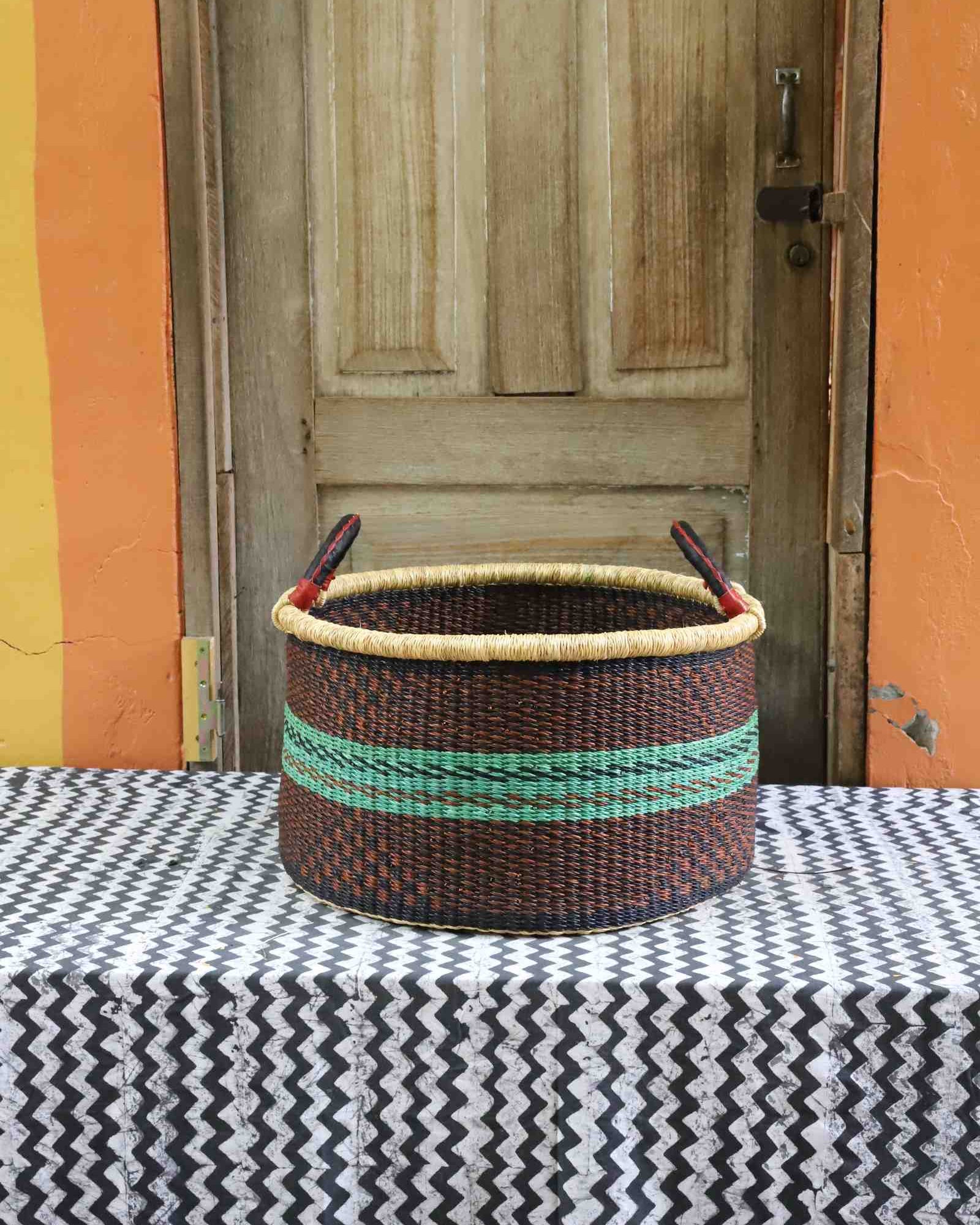 Handwoven Bolga storage basket in dark brown with green horizontal stripes and twin leather-wrapped handles.