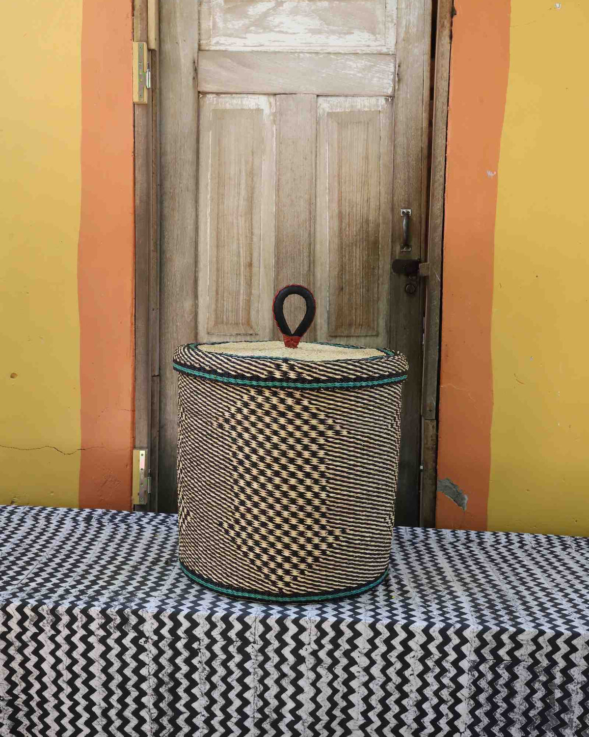 Handwoven Bolga laundry basket with lid in natural straw with a black checkerboard pattern.
