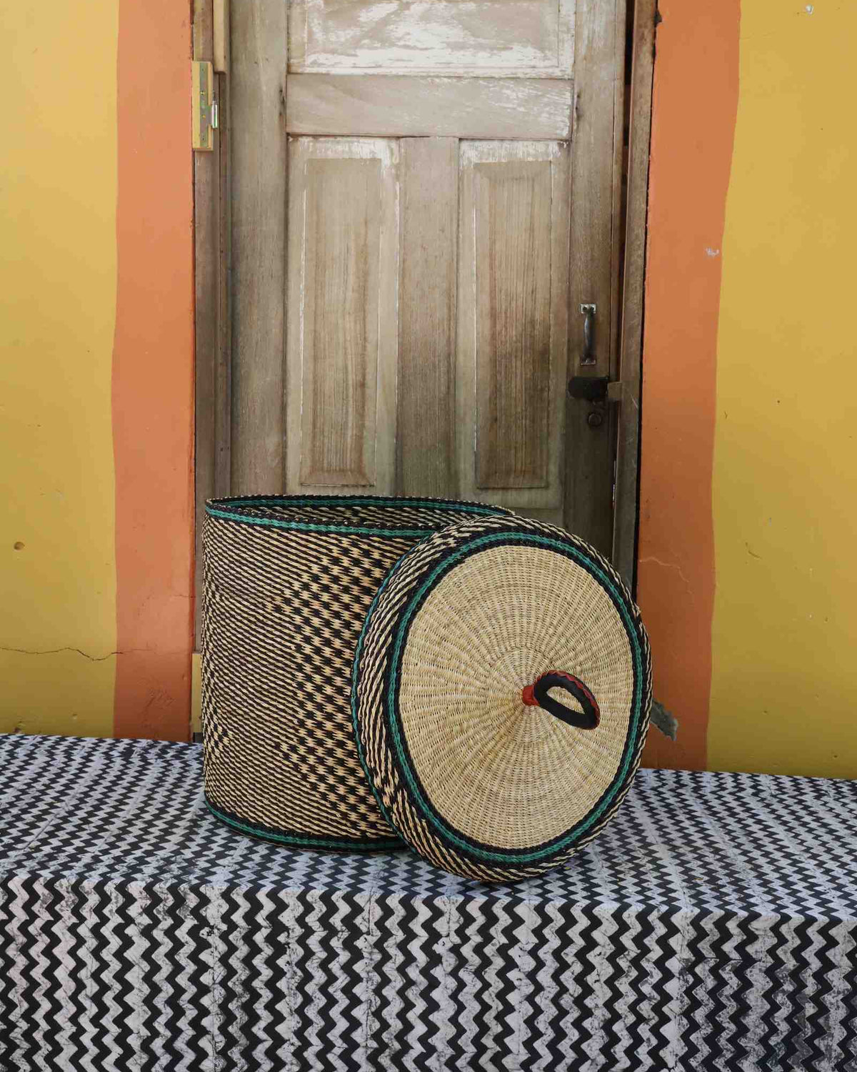 Handwoven Bolga laundry basket with lid removed, natural straw checker body with teal rim accent on the lid.