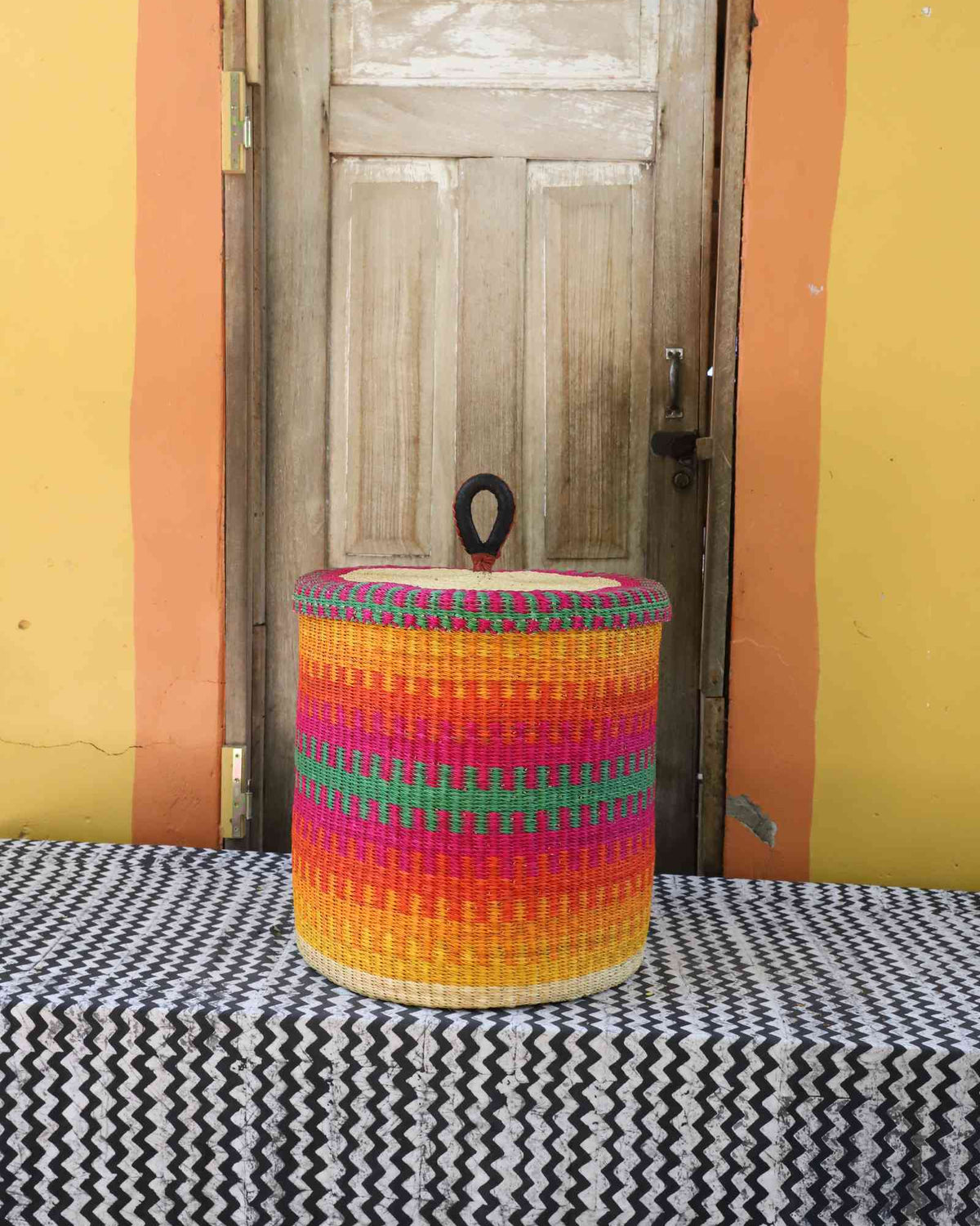 Handwoven Bolga laundry basket with lid in fine multicolour stripes of pink, orange, yellow and green.