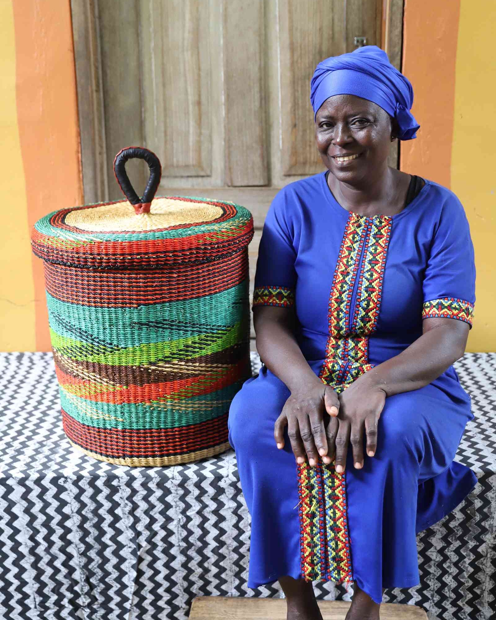 Lidded laundry basket in rust and teal wave-patterned weave, shown beside a seated person for scale.