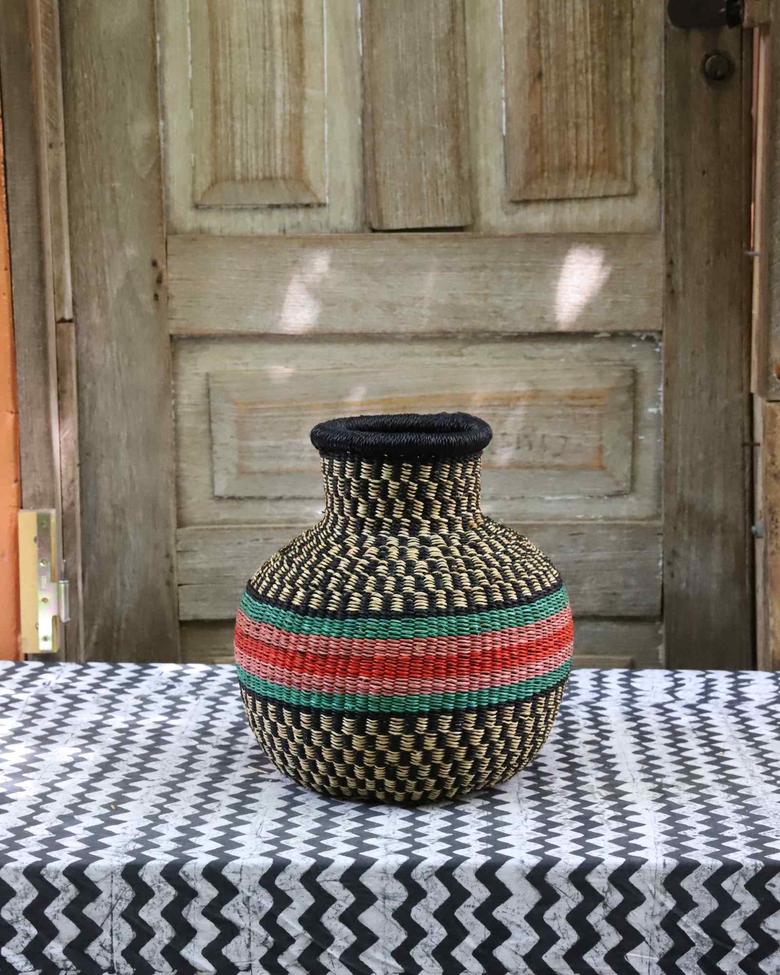 Small vase-shaped Bolga basket in black and cream weave with a red and green striped band, on a tablecloth.