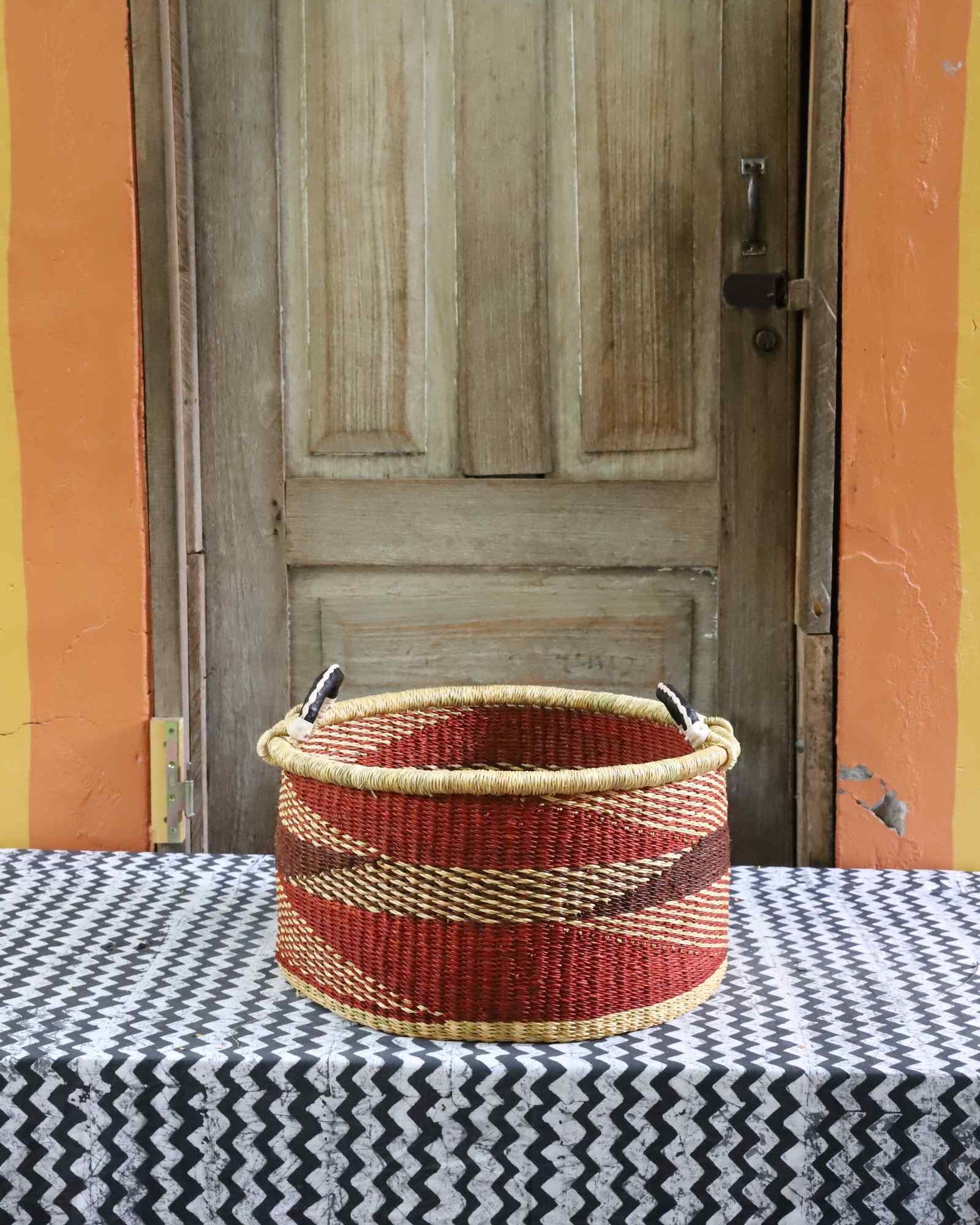 Handwoven Bolga basket in natural straw with red and burgundy geometric stripes and twin leather-wrapped handles.