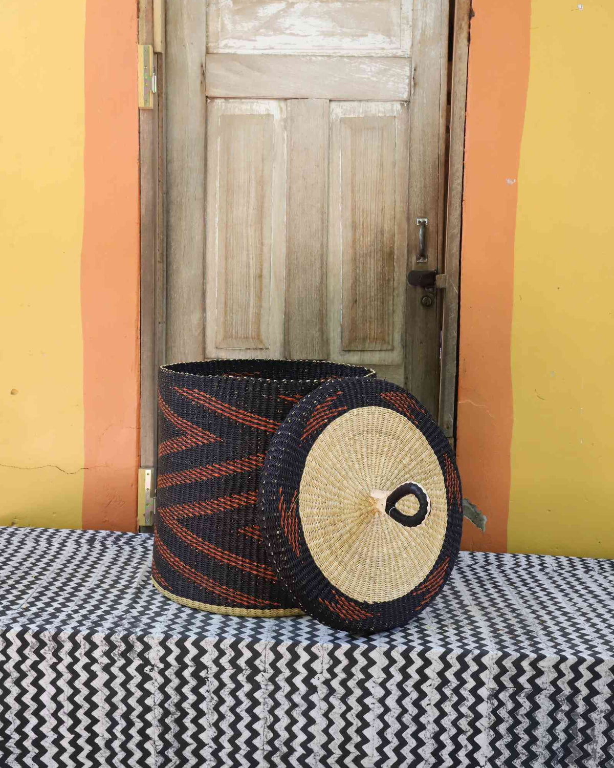 Handwoven Bolga laundry basket with lid removed, dark blue body with rust-orange zigzag pattern and lid.