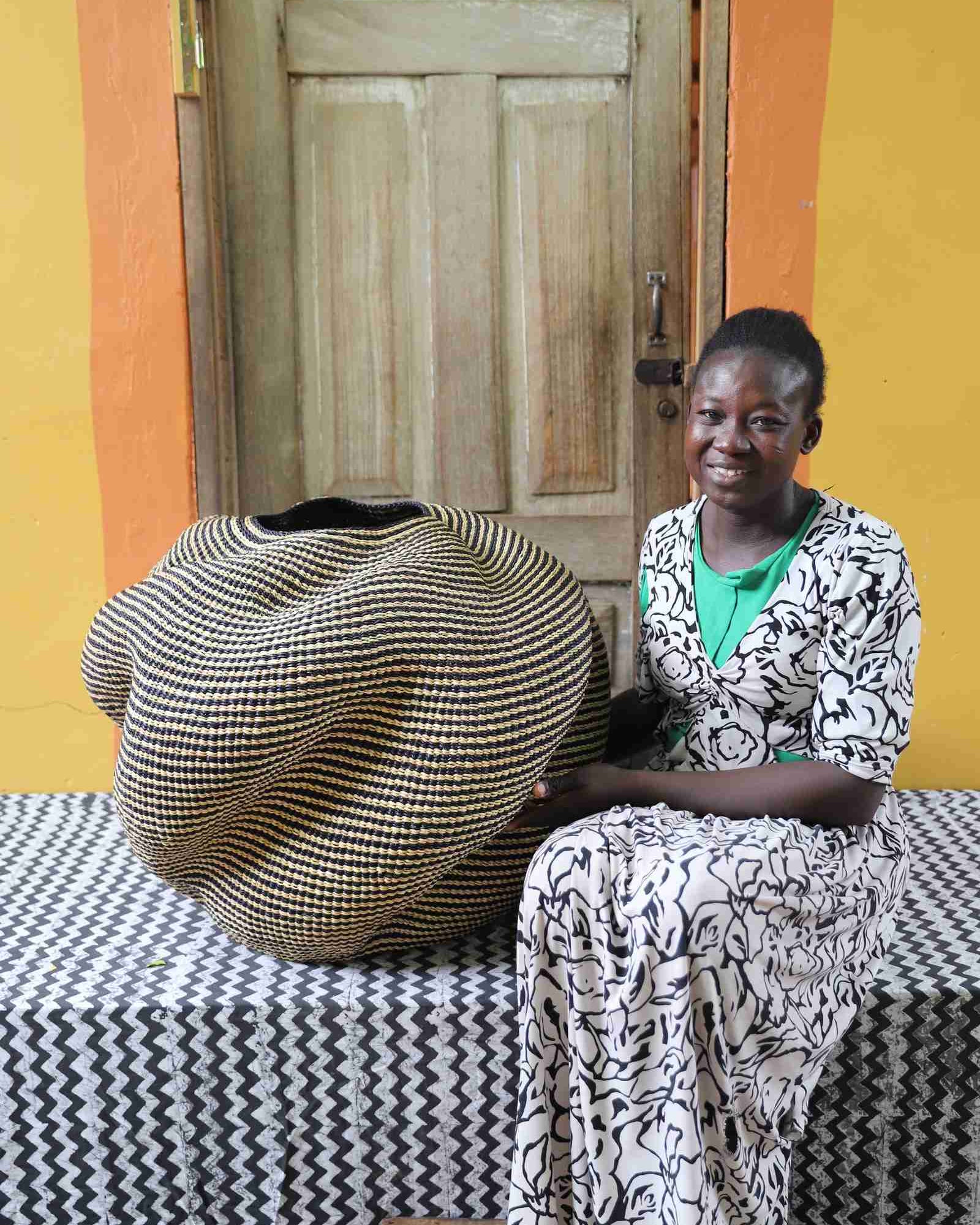 Large nest-shaped Bolga art basket in natural straw, shown beside a seated person for scale.
