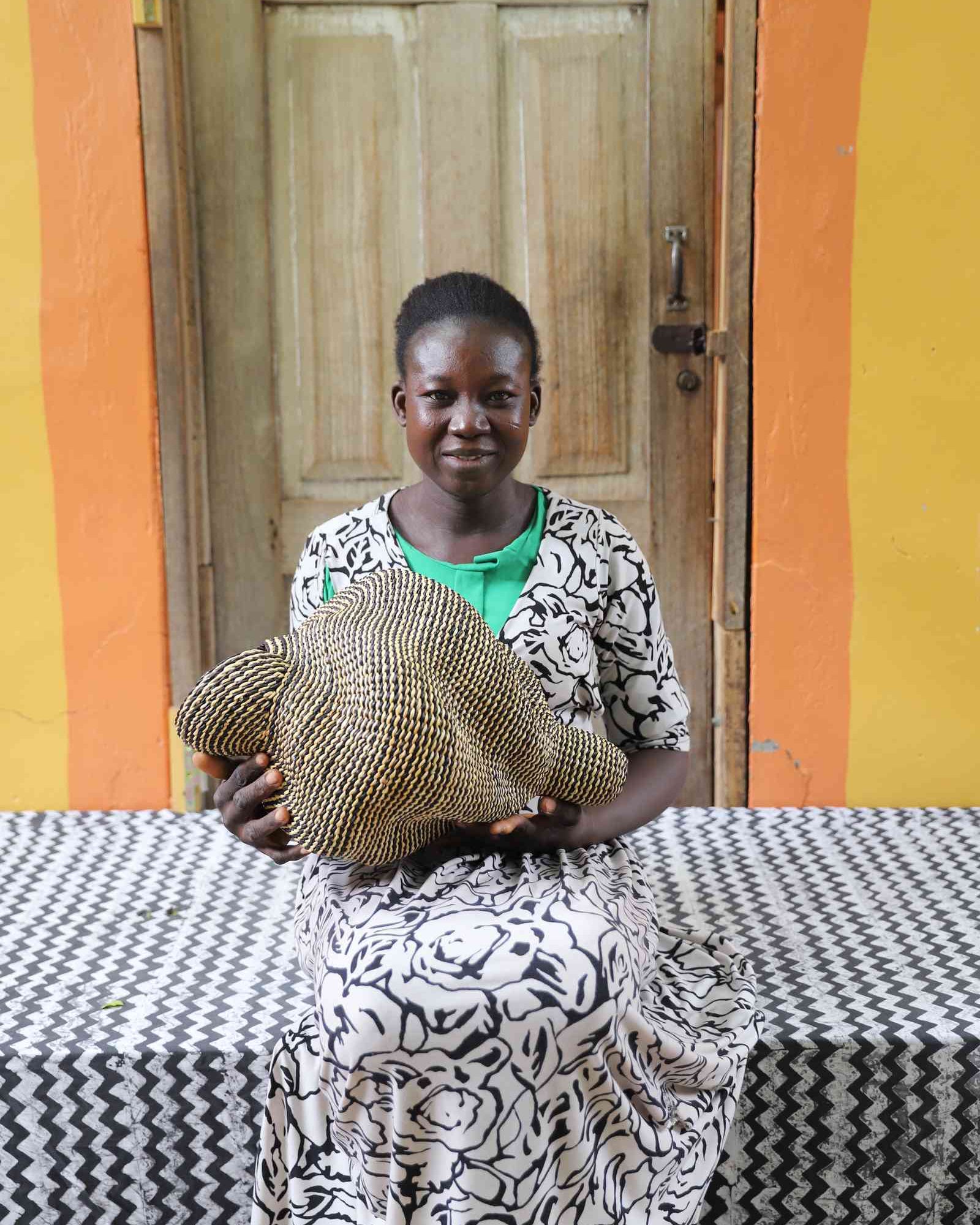 Small spiral-form Bolga art basket in natural straw, held by a seated person for scale.