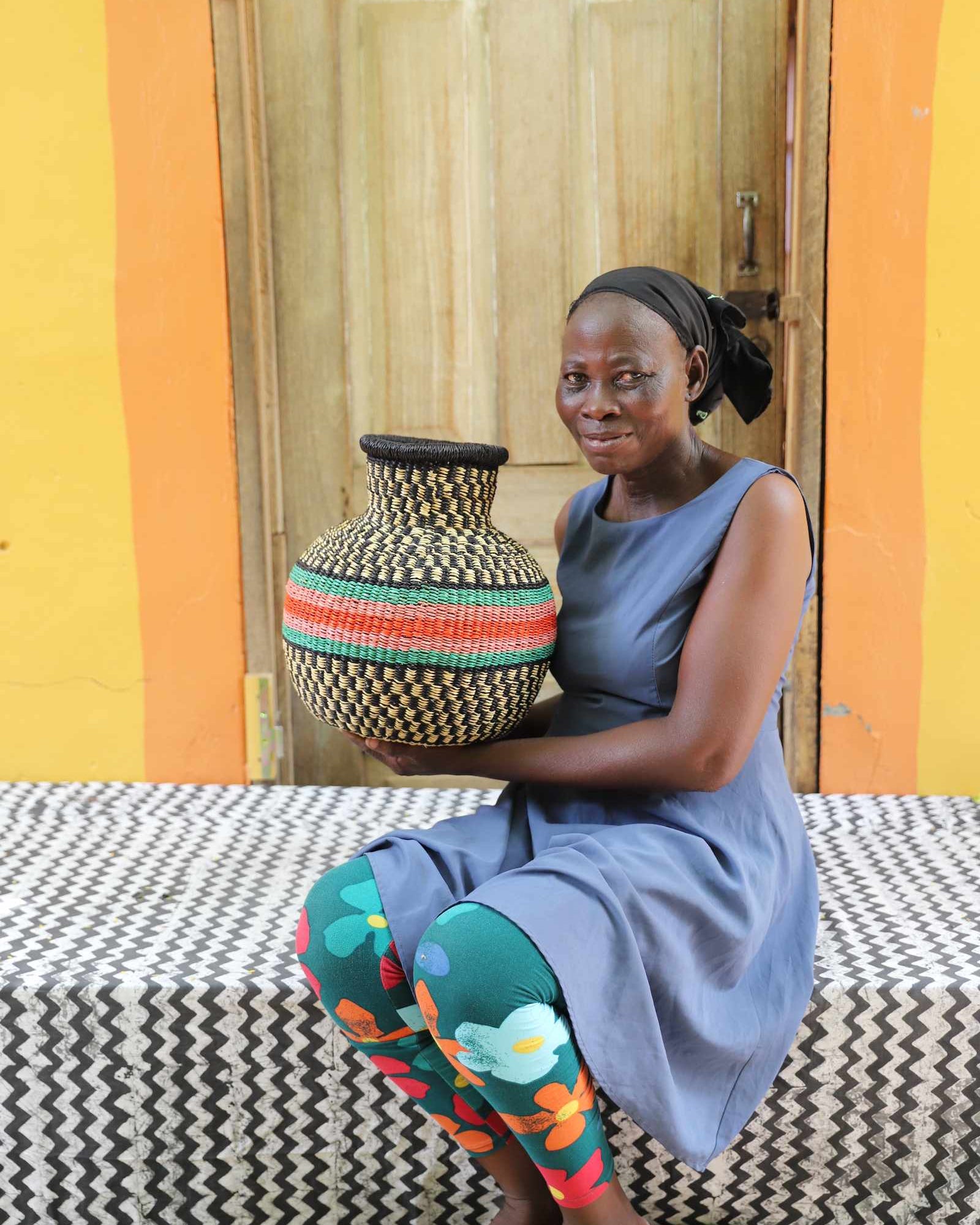 Small vase-shaped Bolga basket with a red and green striped band, held by a seated woman for scale.