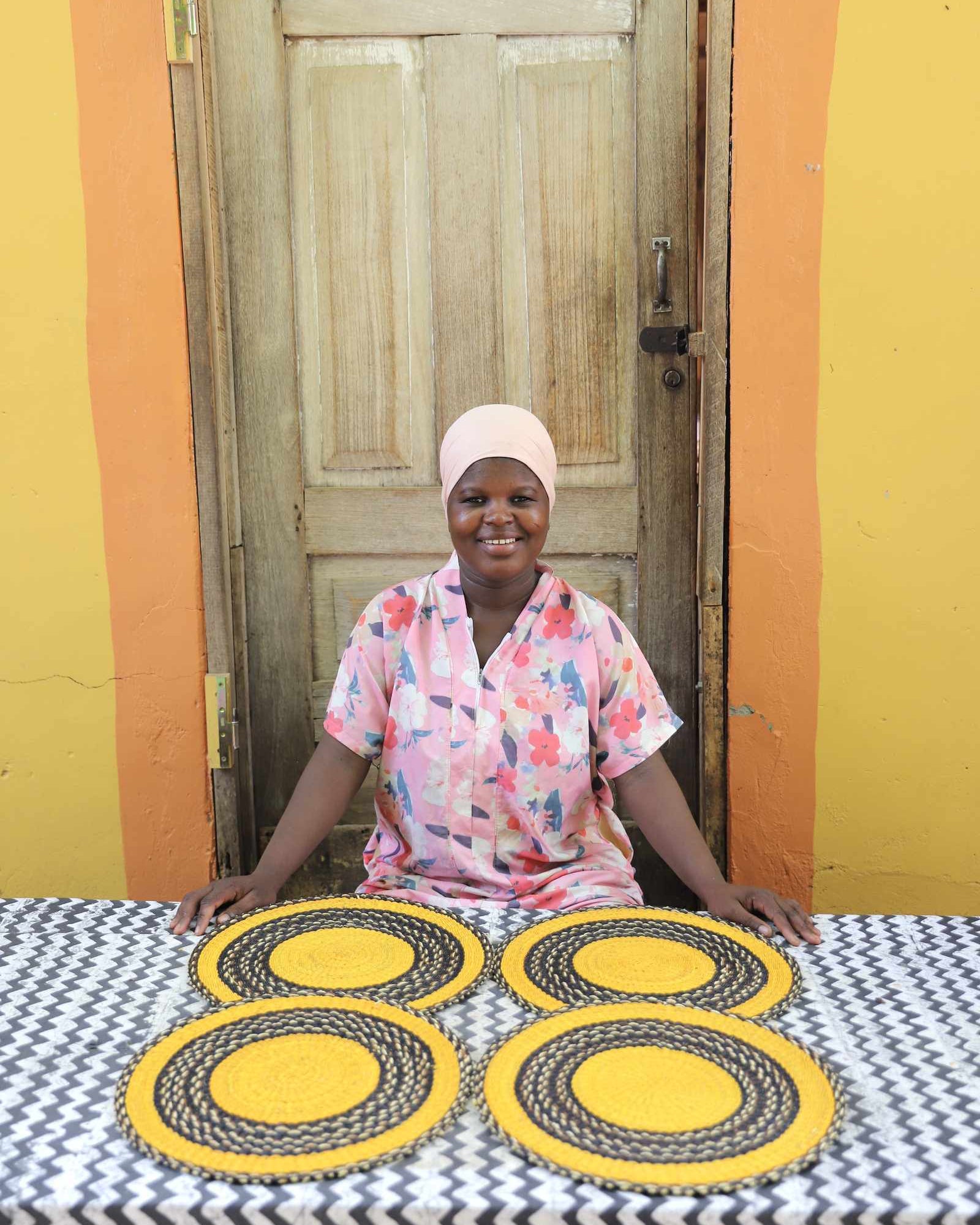 Set of four handwoven Bolga placemats in natural straw with black border rings, displayed by their maker in Ghana.