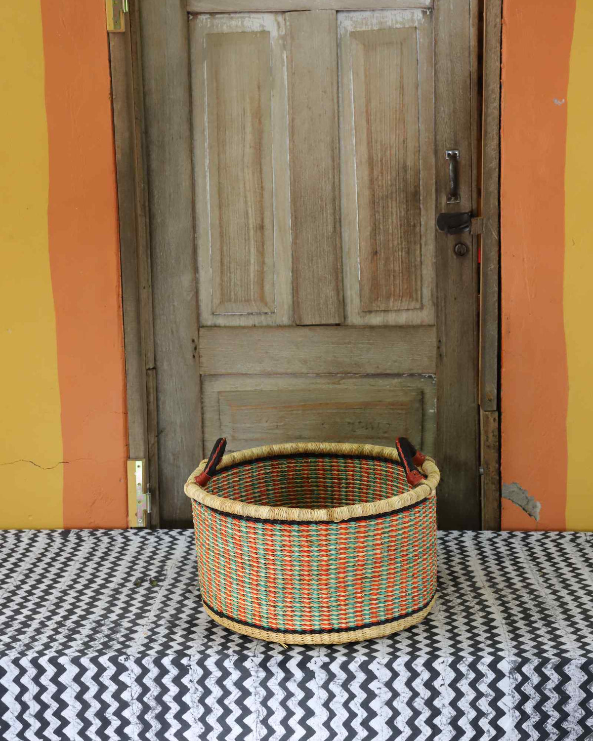Small handwoven Bolga storage tub in natural straw with orange and green banded stripes.