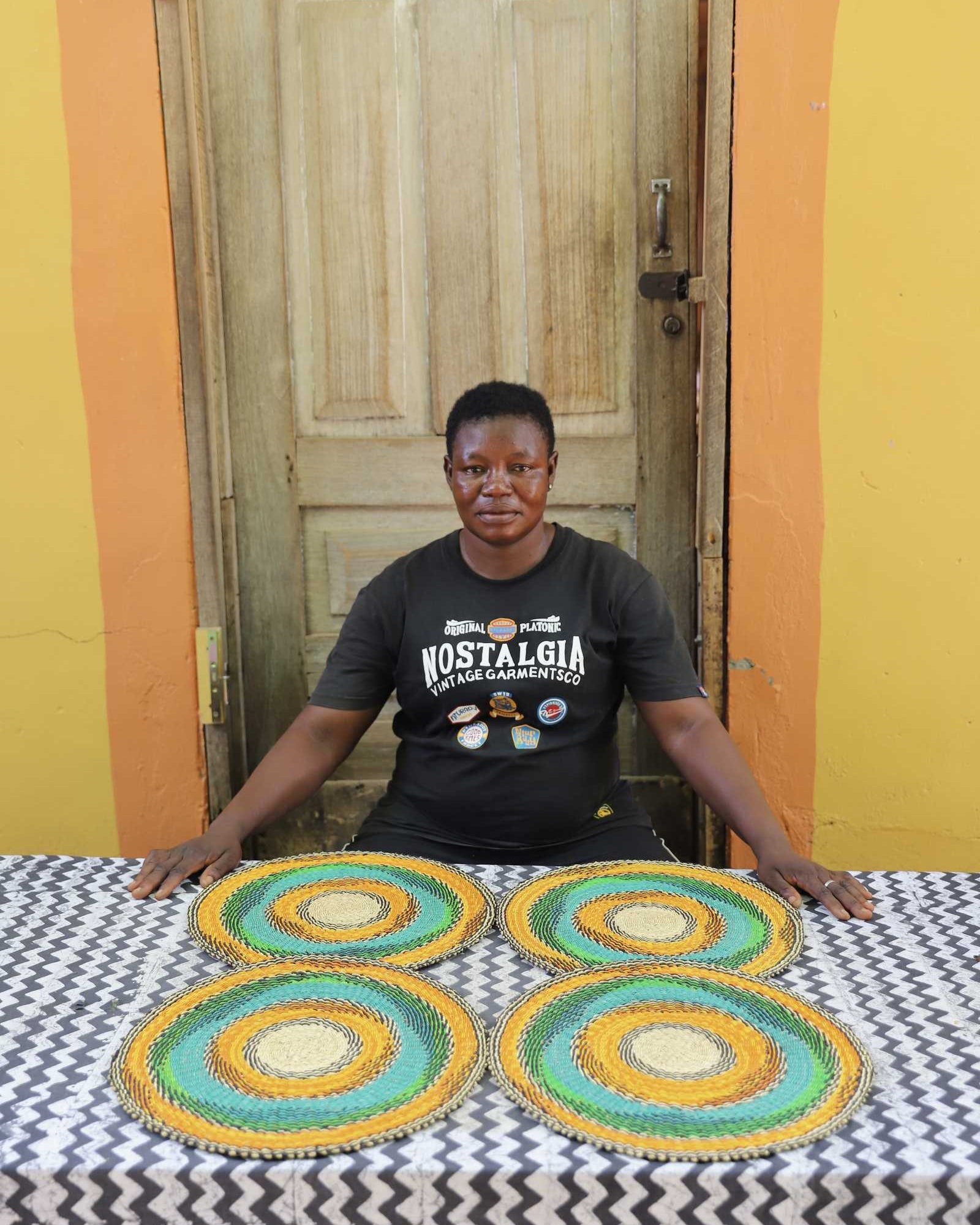 Set of four handwoven Bolga placemats with concentric rings in orange, teal and green, displayed in Ghana.