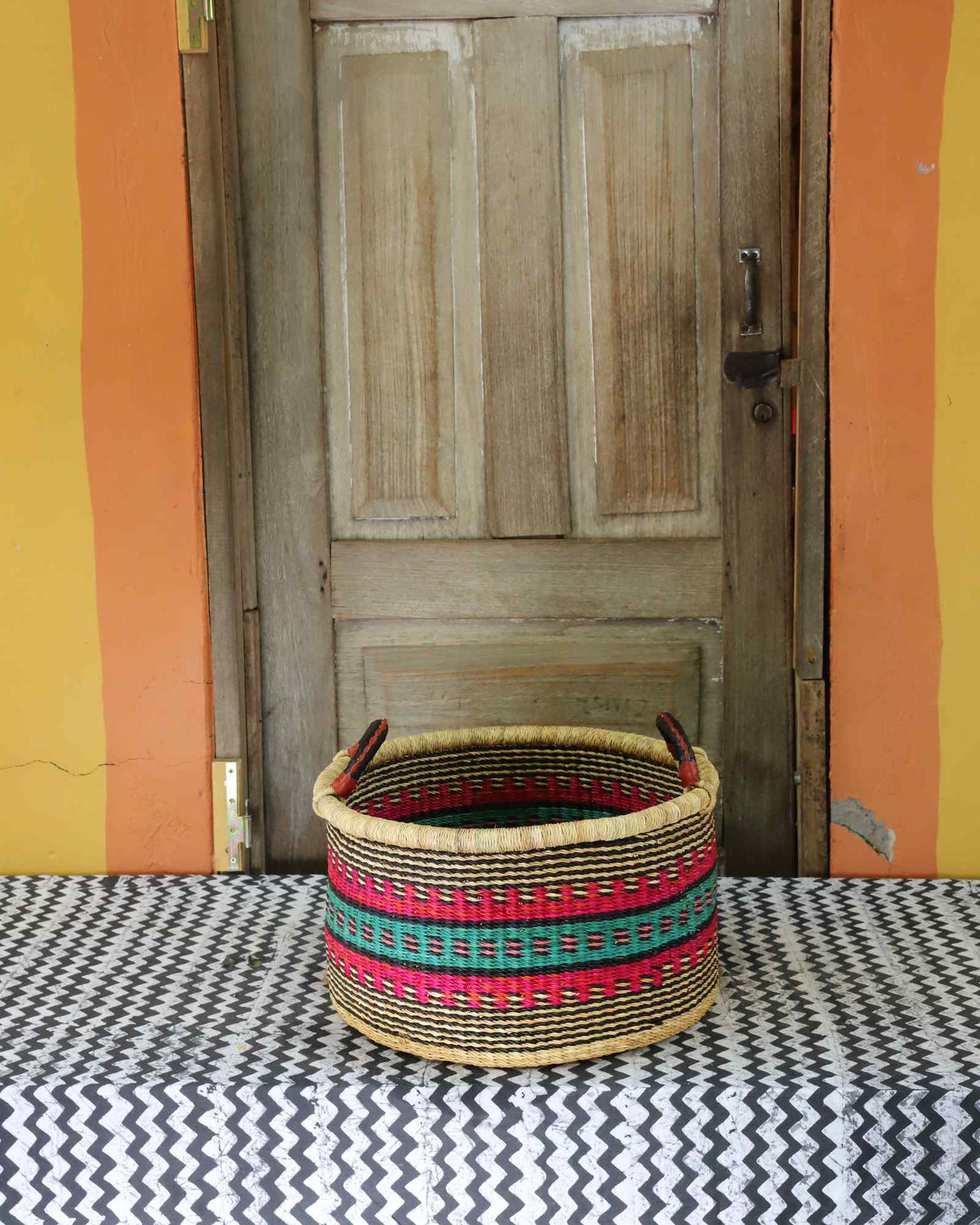 Small handwoven Bolga storage tub in natural straw with red, green and yellow banded stripes.