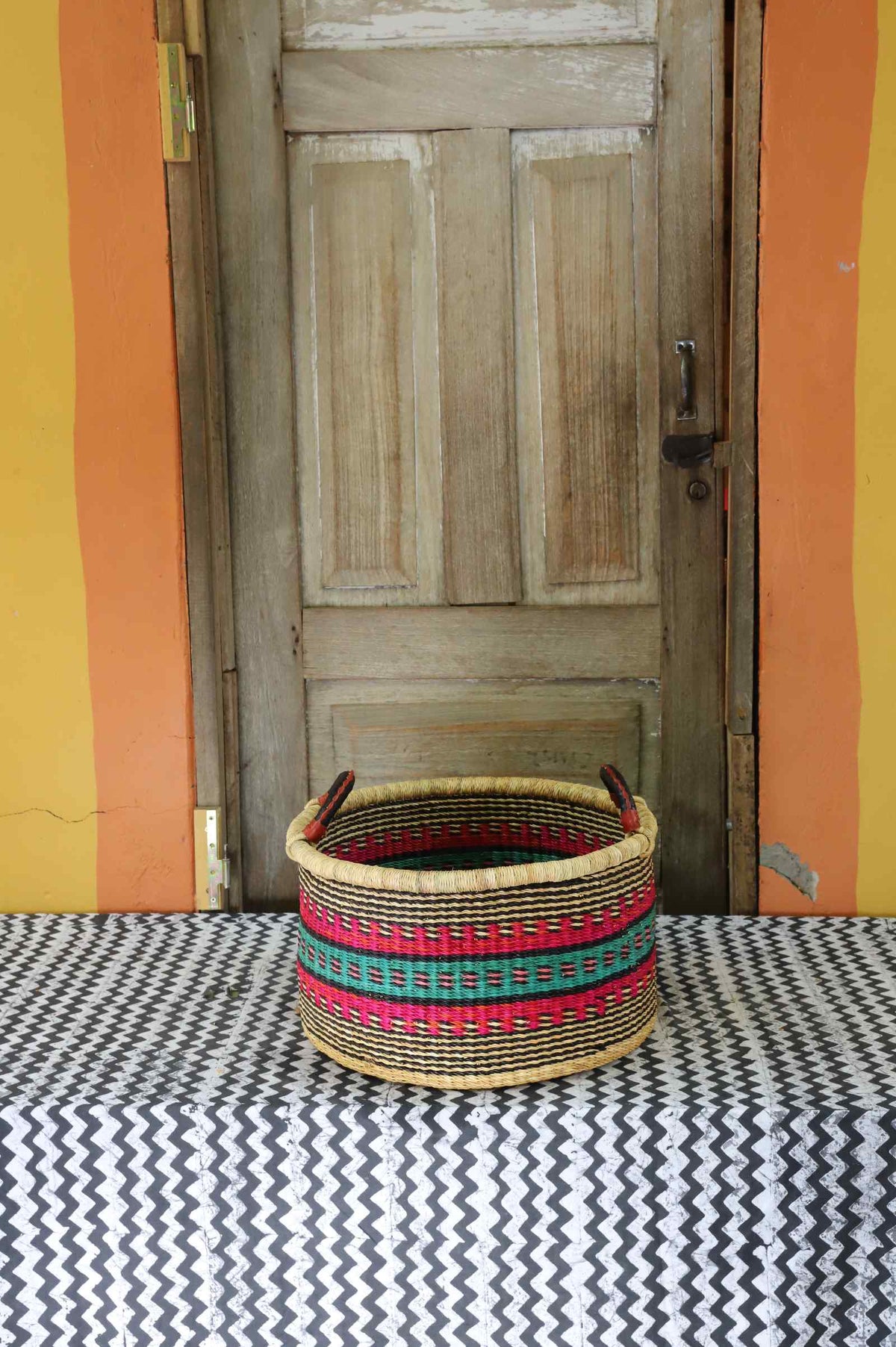 Small handwoven Bolga storage tub in natural straw with red, green and yellow banded stripes.